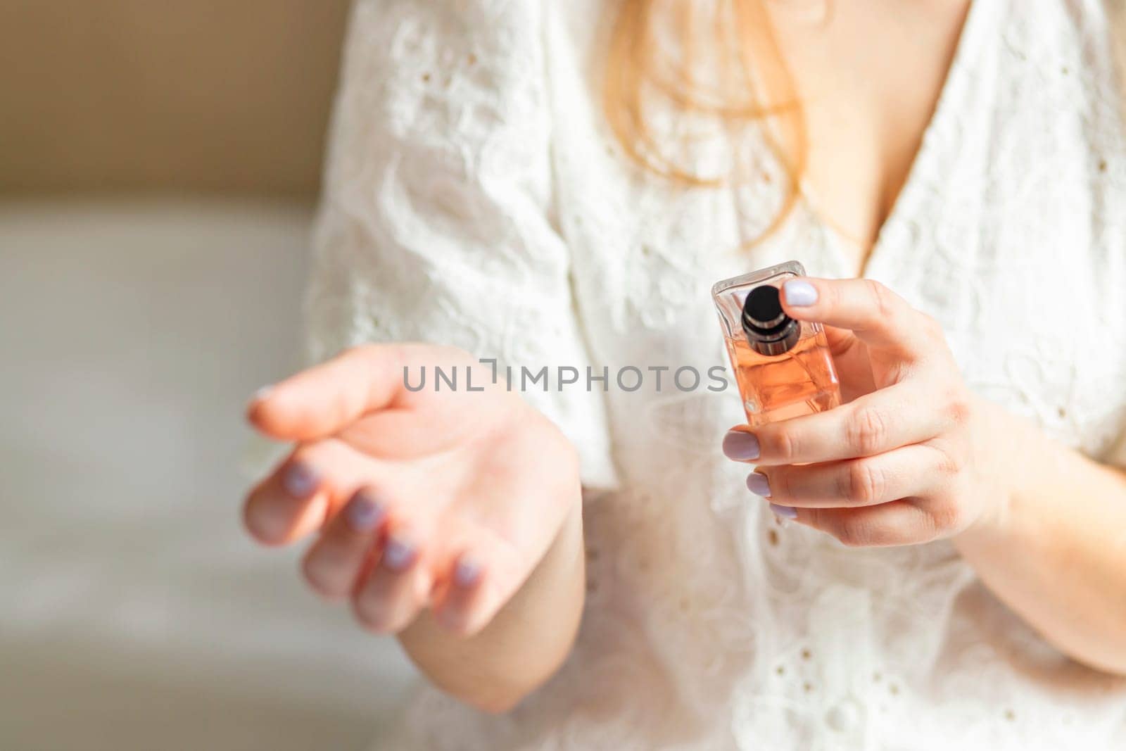 Beautiful young woman using perfume at home.