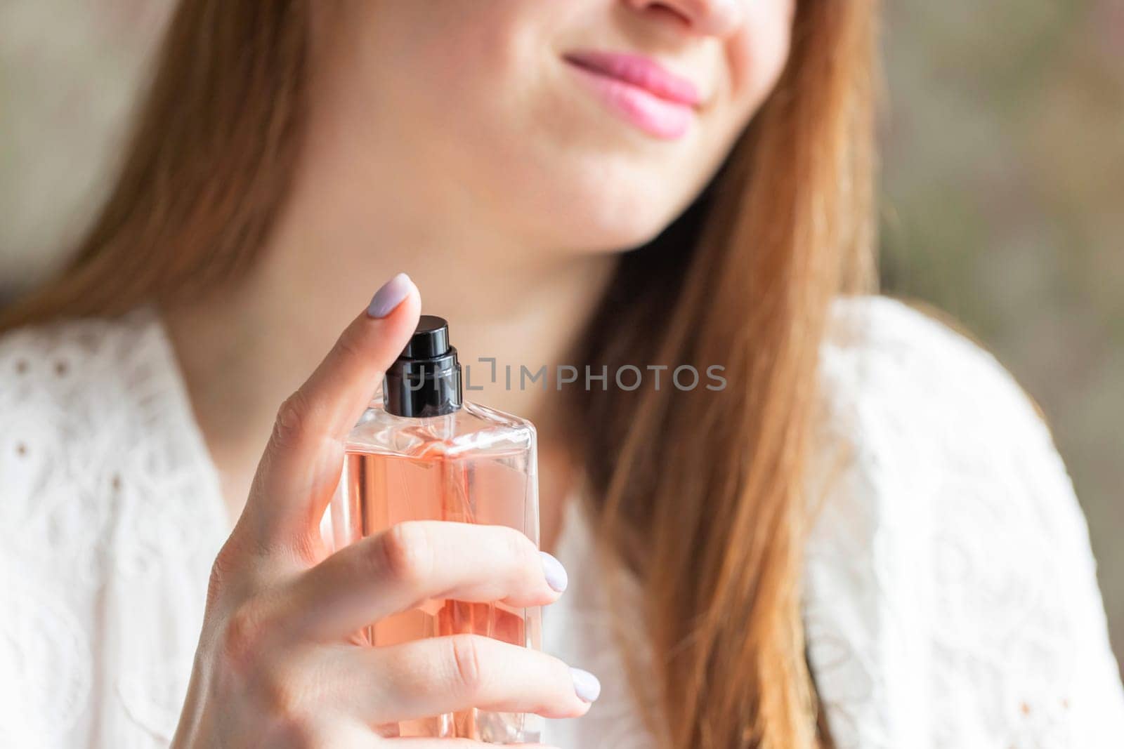 Beautiful young woman with bottle of perfume spraying it on her neck at home.