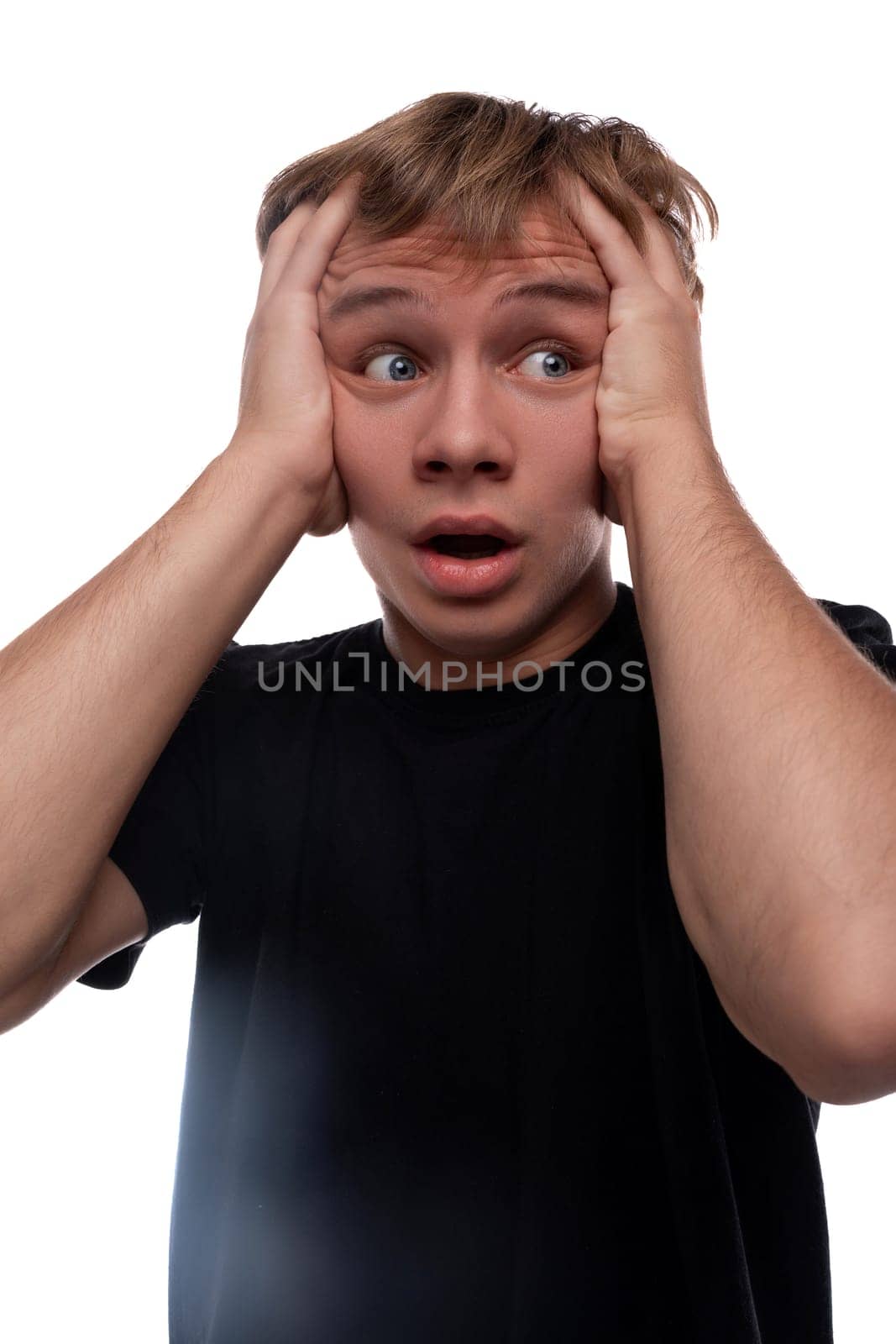 Worried young man with blond hair in a black T-shirt thinks about problems and holds his head.