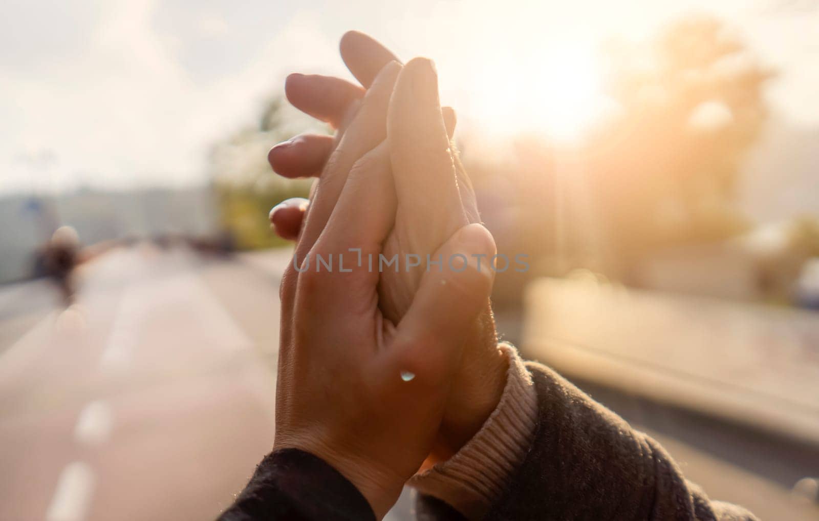 A gentle touch, a man's hand to a woman's hand, an elderly couple holding hands together on a walk in the park in the sun, the husband cares and supports his wife.