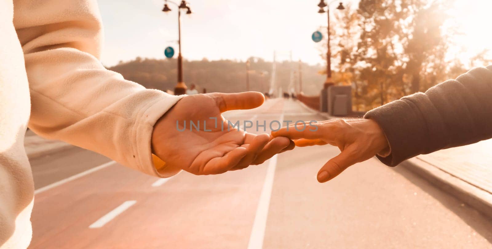 Сouple holding hands, with love and care support each other and walk together in the park on a sunny day, lead an active healthy lifestyle. A man holds the hand of a beloved wife.