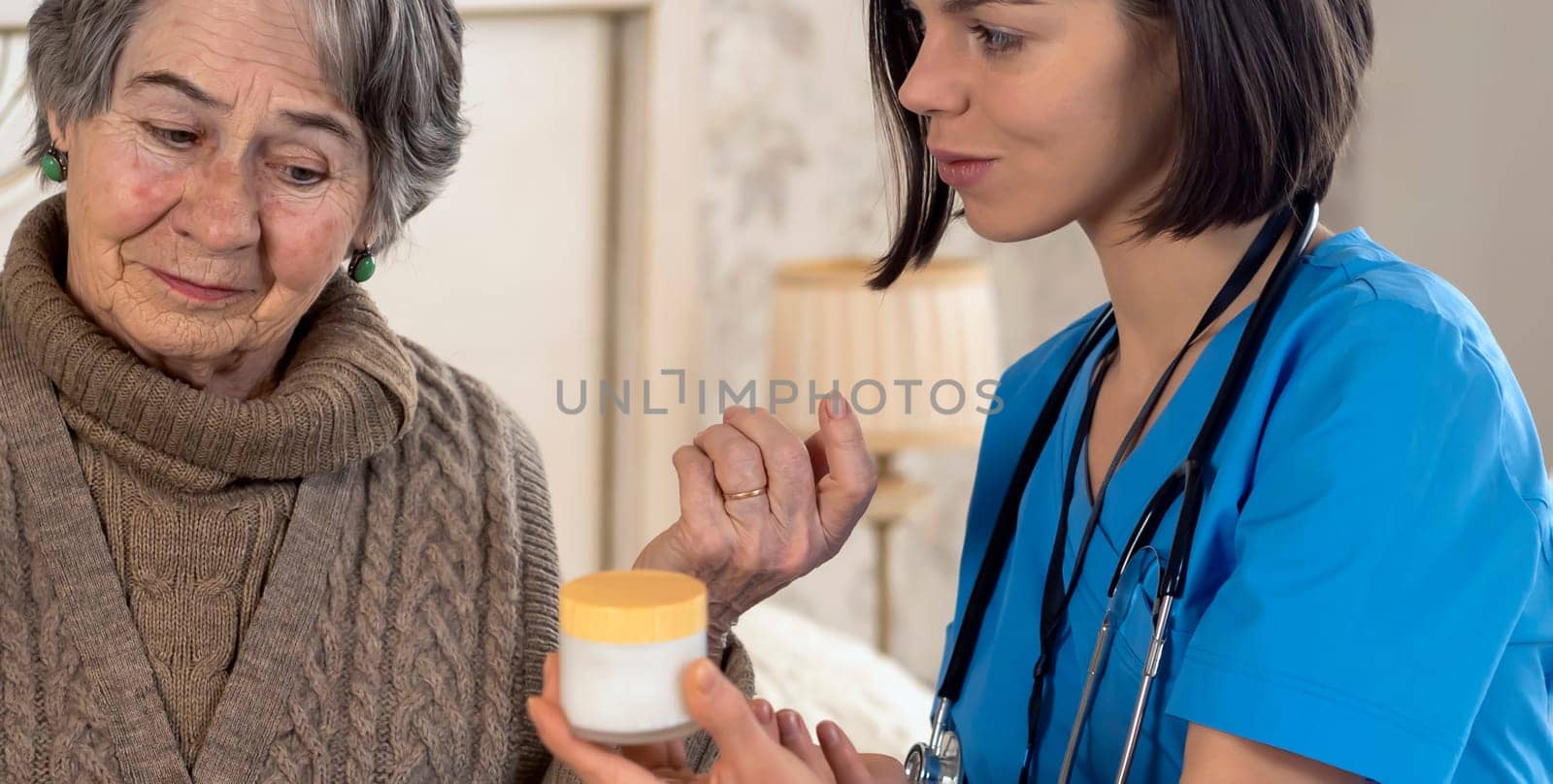 A smiley young nurse takes care of an elderly 80-year-old woman at home, helps with a threatment. Happy retired woman and trust between doctor and patient. Medicine and healthcare.