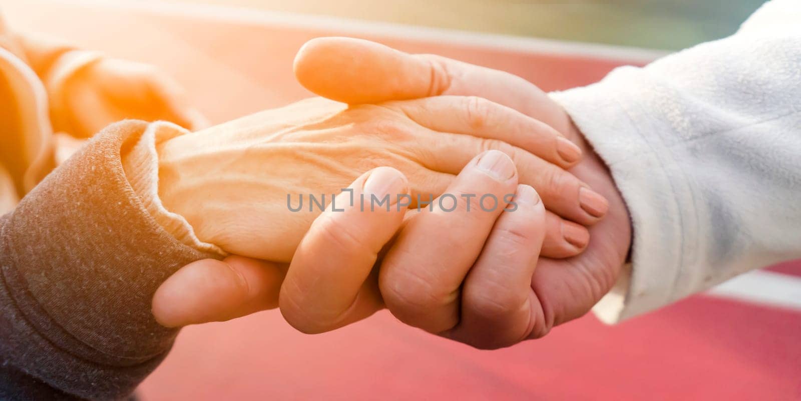 A man, a husband carefully holds his beloved grandmother or wife, supports and helps an elderly retired woman, grandparents together. Male and female elderly hands with wrinkles closeup in the sun.
