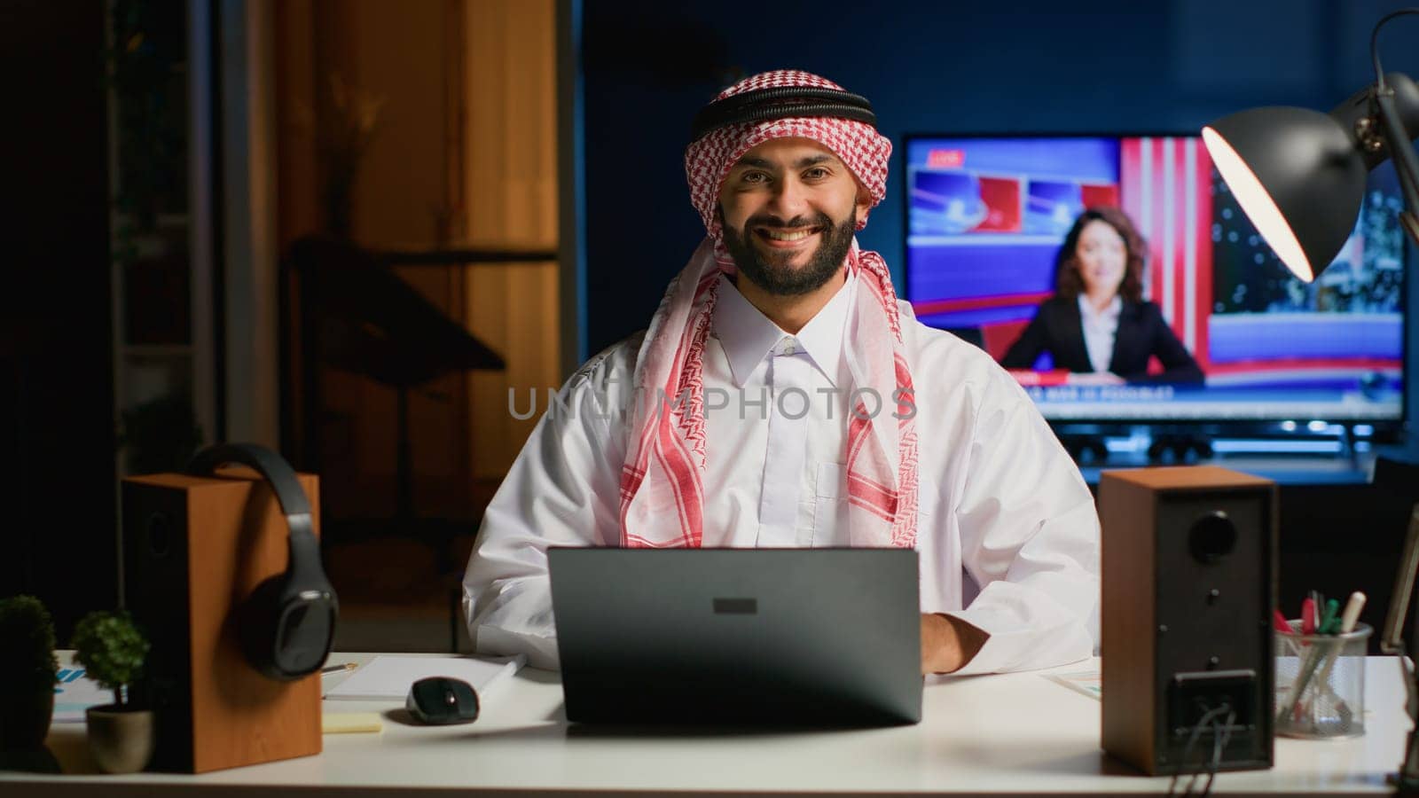 Portrait of smiling Arab businessman working at modern desk, typing on his laptop, solving tasks. Muslim guy browsing on digital device, doing email communication in professional office setting