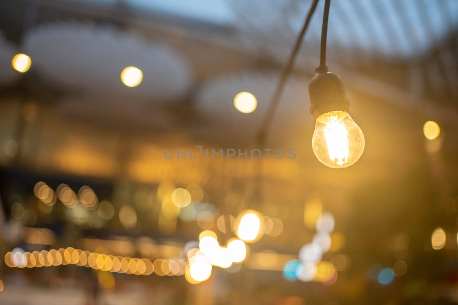 Light bulb decoration Event Festival outdoor. Holiday blur background. Close-up of outdoor garland with warm lights, with blurred bridge on background. Night festival abstract photo of garland