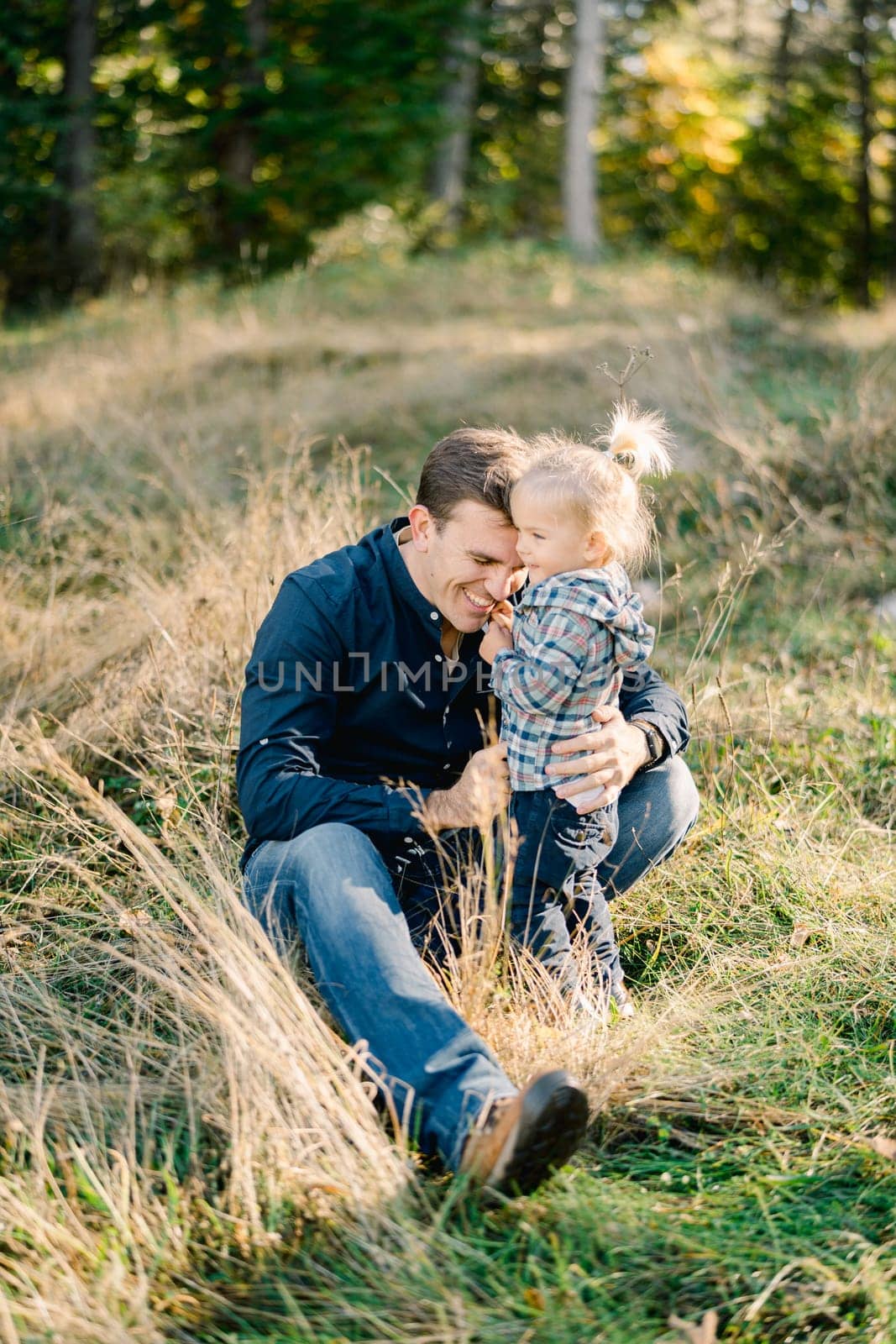 Sitting dad hugging a little girl standing next to him in a clearing in the forest. High quality photo