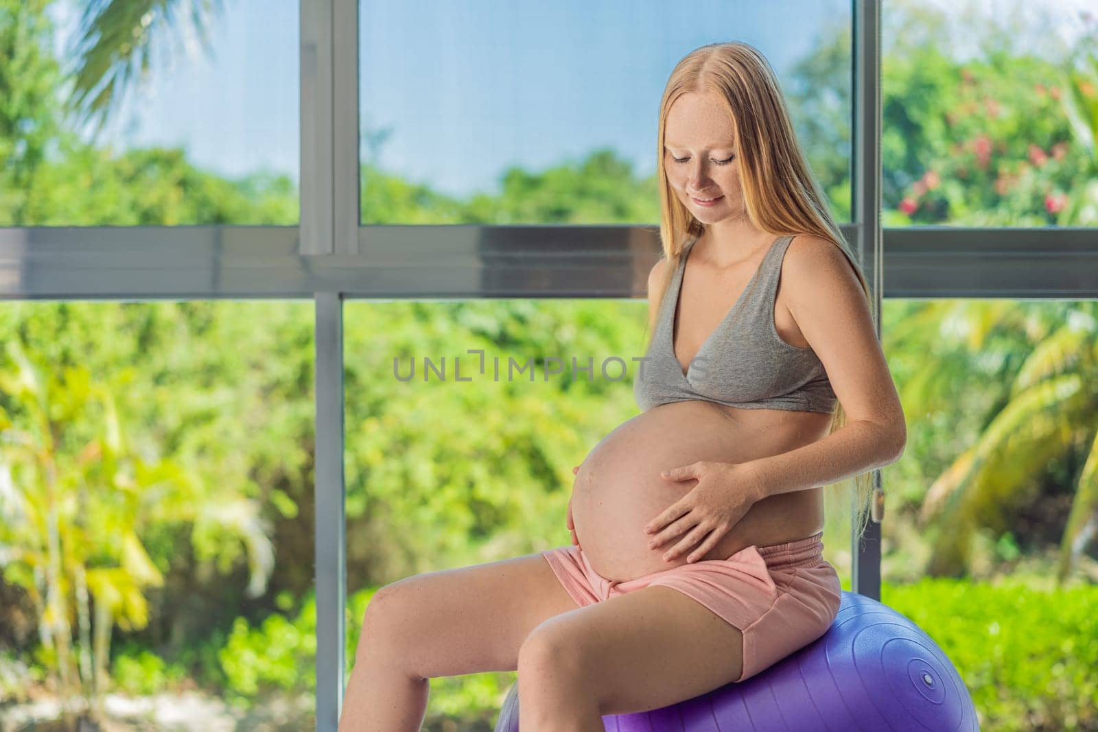 Pregnant woman exercising on fitball at home. Pregnant woman doing relax exercises with a fitness pilates ball. Against the background of the window.