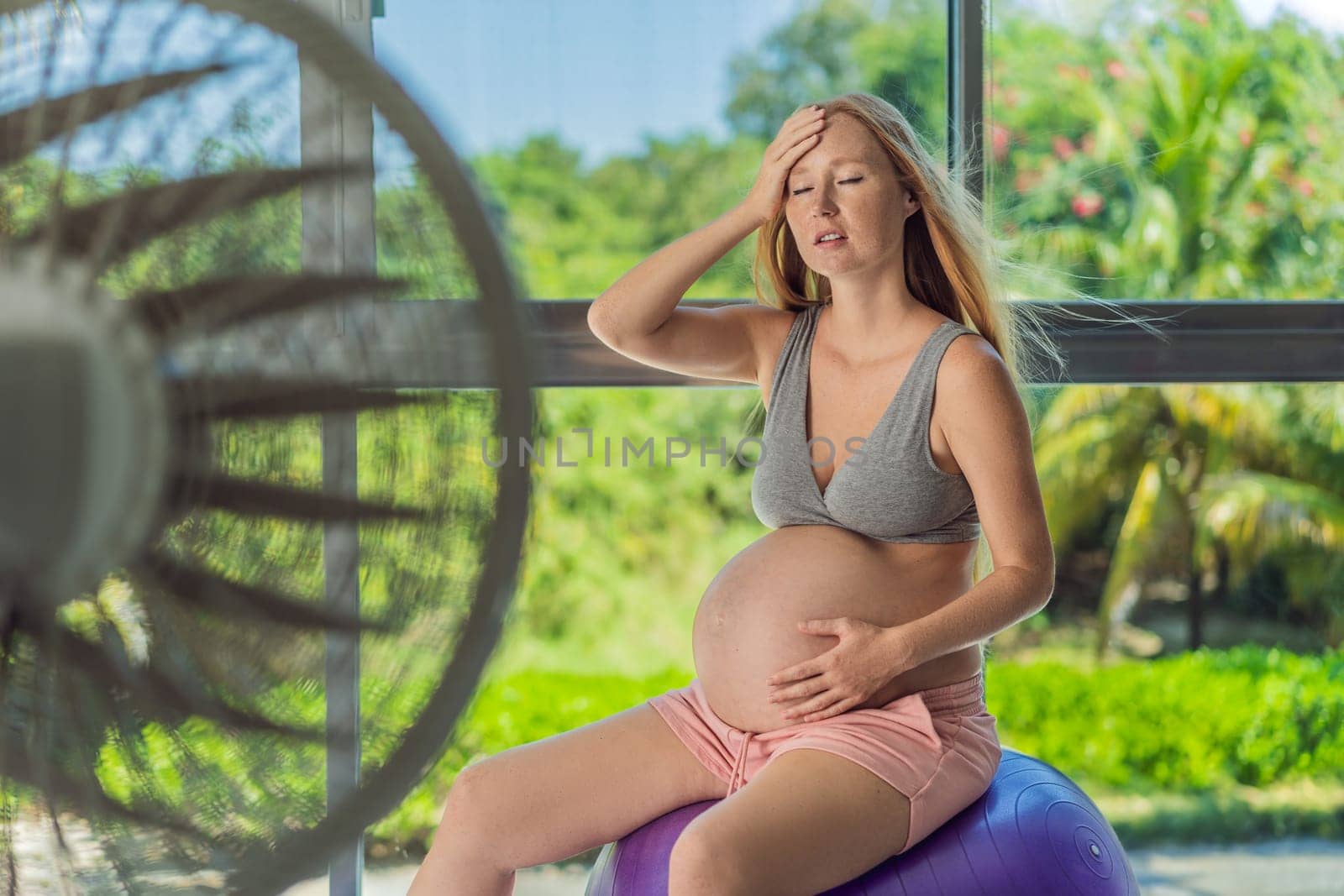 A pregnant woman seeks relief from an abnormal heatwave by using a fan, ensuring her comfort and well-being during sweltering conditions by galitskaya