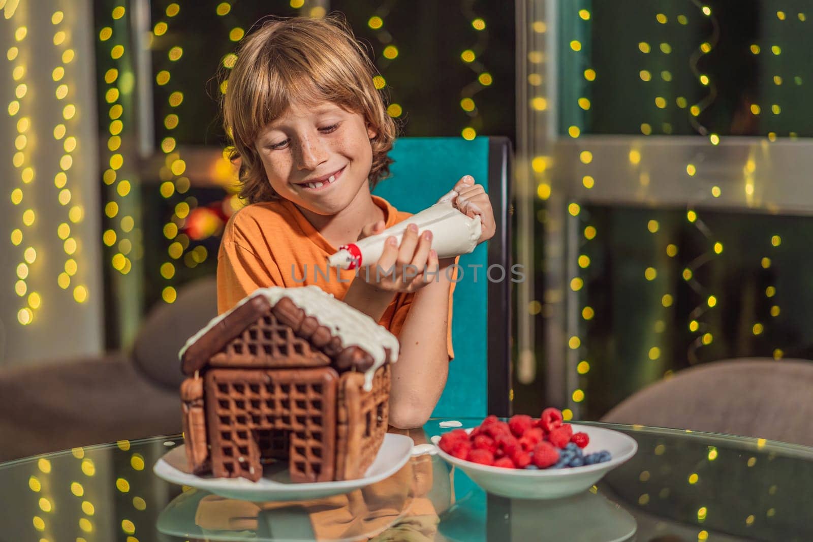 Immerse in festive delight as a boy crafts boy crafting an unconventional gingerbread house, infusing Christmas with unique creativity and festive cheer. A sweet scene of seasonal bonding and culinary fun by galitskaya