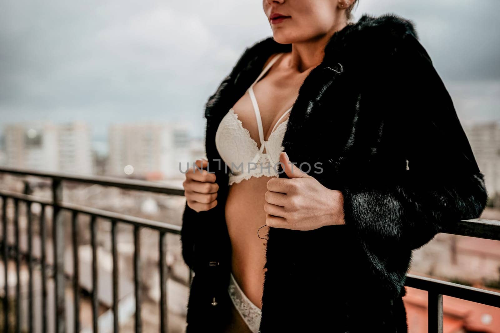 Unrecognizable Young sexy brunette woman in lingerie and fur coat staying on balcony and posing. Close-up of a woman's bust, frozen with goosebumps. Flirting of lovely female in hotel room. by panophotograph