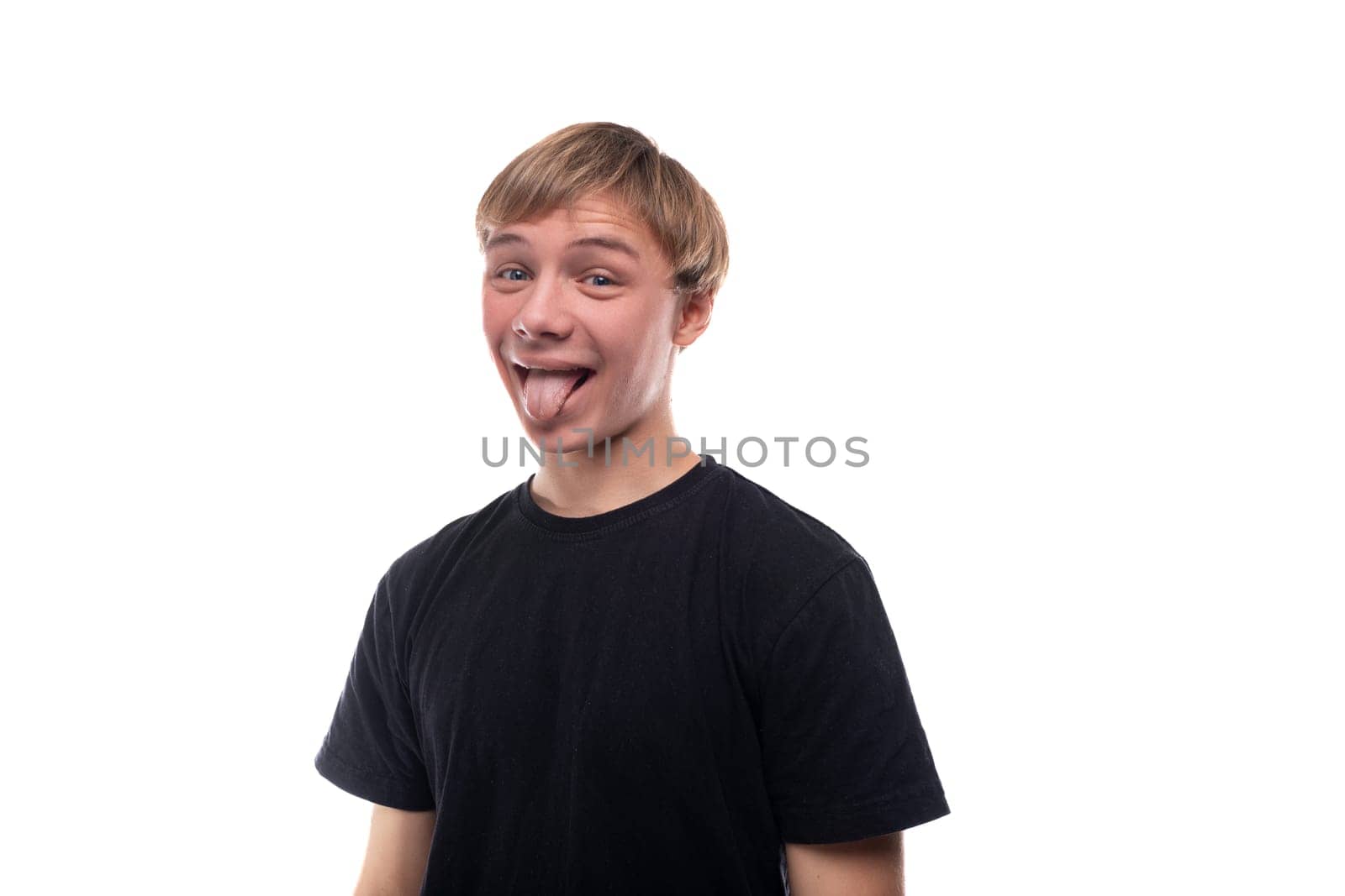 Funny fair-haired teenager guy in a black T-shirt shows his tongue.