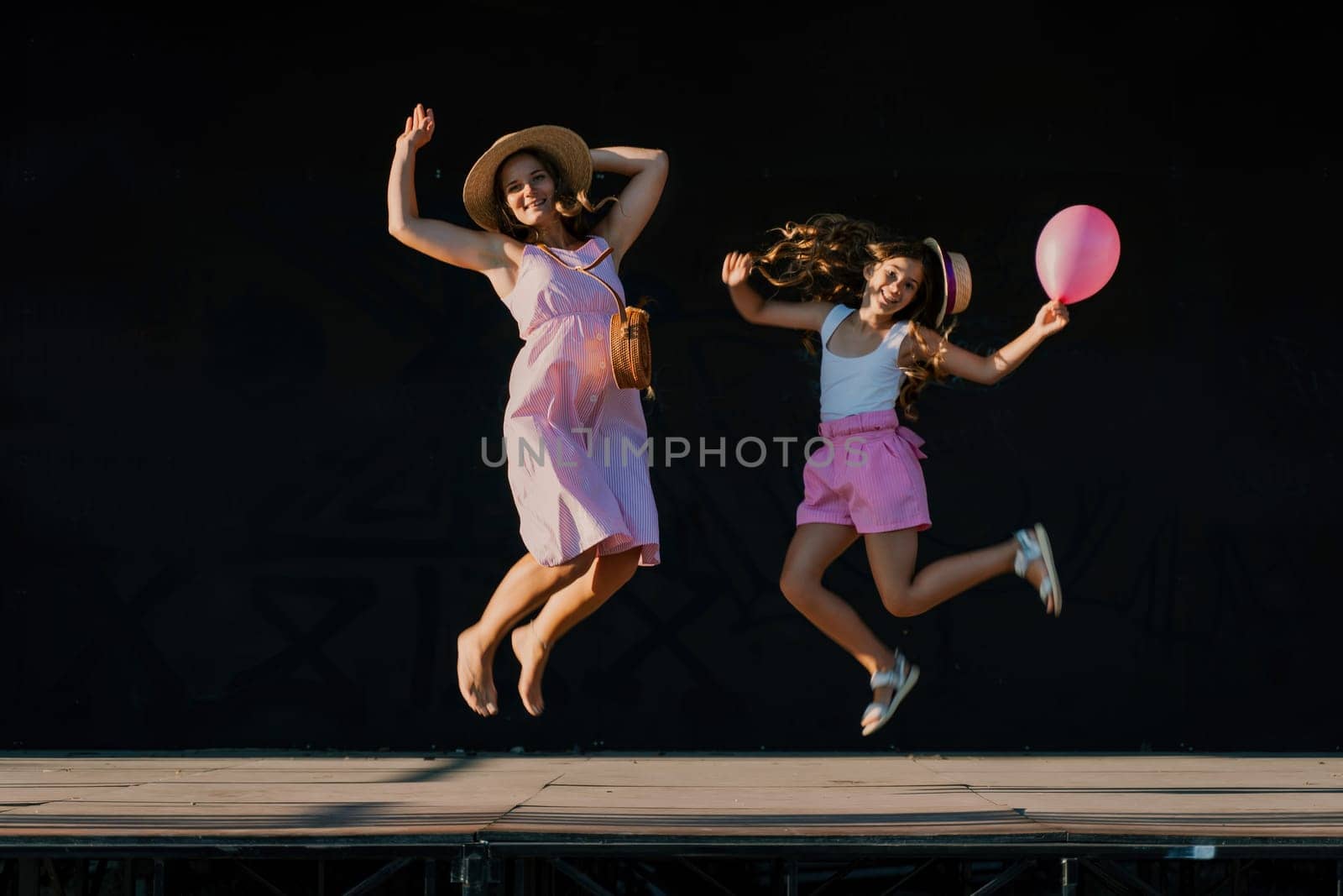 mother and daughter jumping in pink dresses with loose long hair on a black background. Enjoy communicating with each other by Matiunina