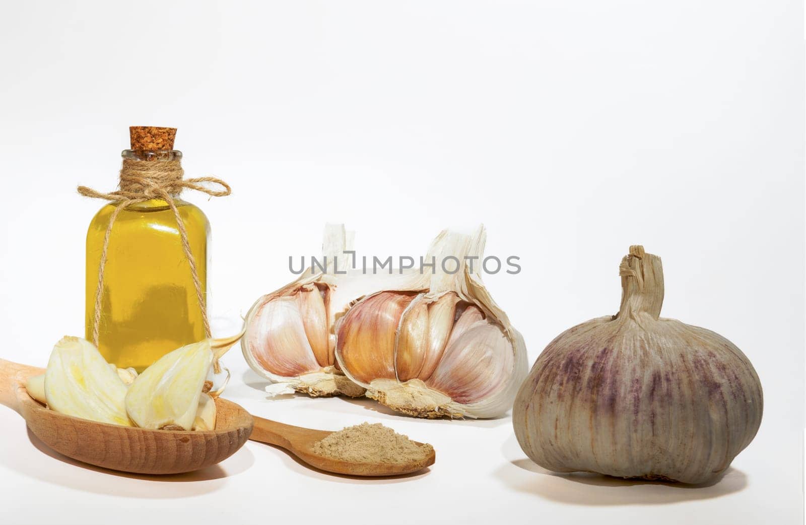 whole, powdered and chopped garlic on a white background with a glass bottle with olive oil