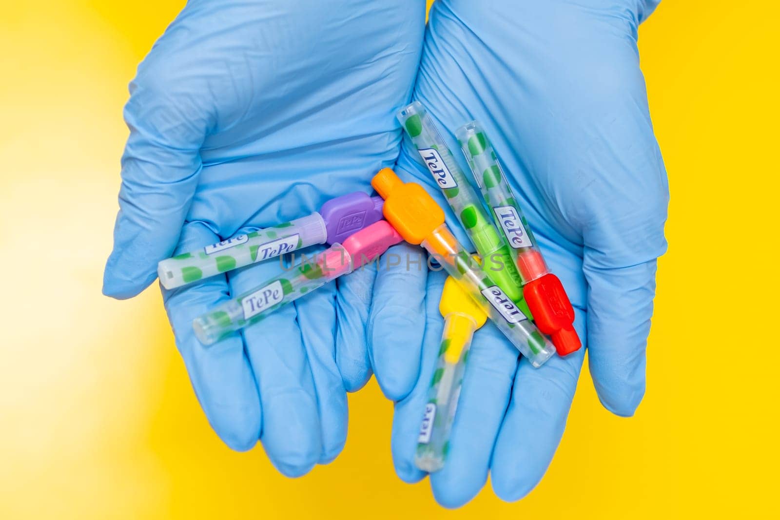 Close up Interdental Toothbrushes in dentists hands in rubber gloves on yellow background, December 2023, Prague, Czech Republic