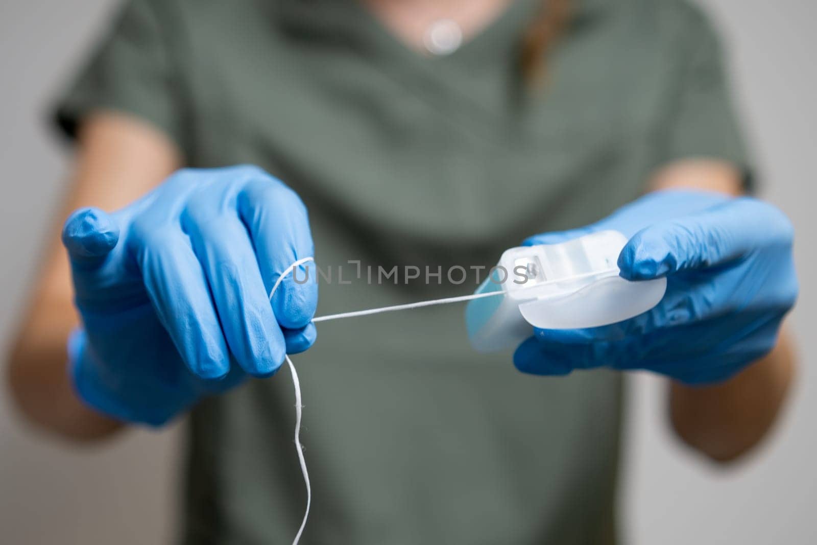 Oral thread or dental floss held by a dental professional wearing rubber gloves.