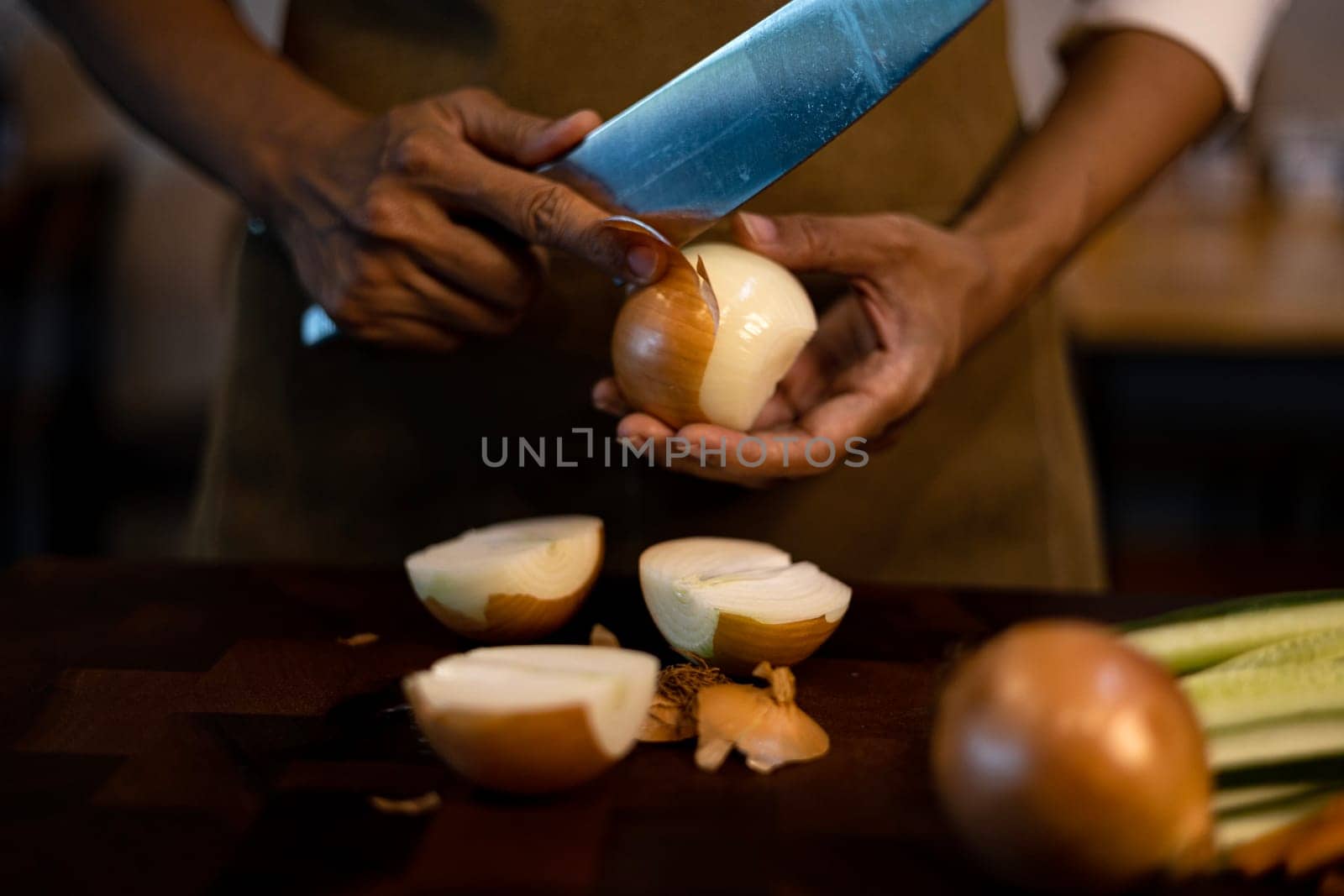Women's hands with a sharp knife peeling white onions in the kitchen.
