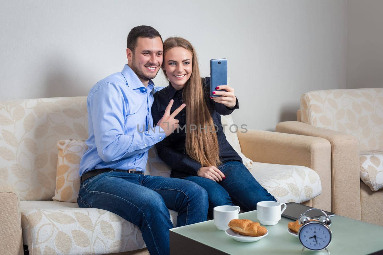 Beautiful young man and woman doing selfie with telephone camera, happy people taking picture smiling to the camera, bvsitting on a sofa