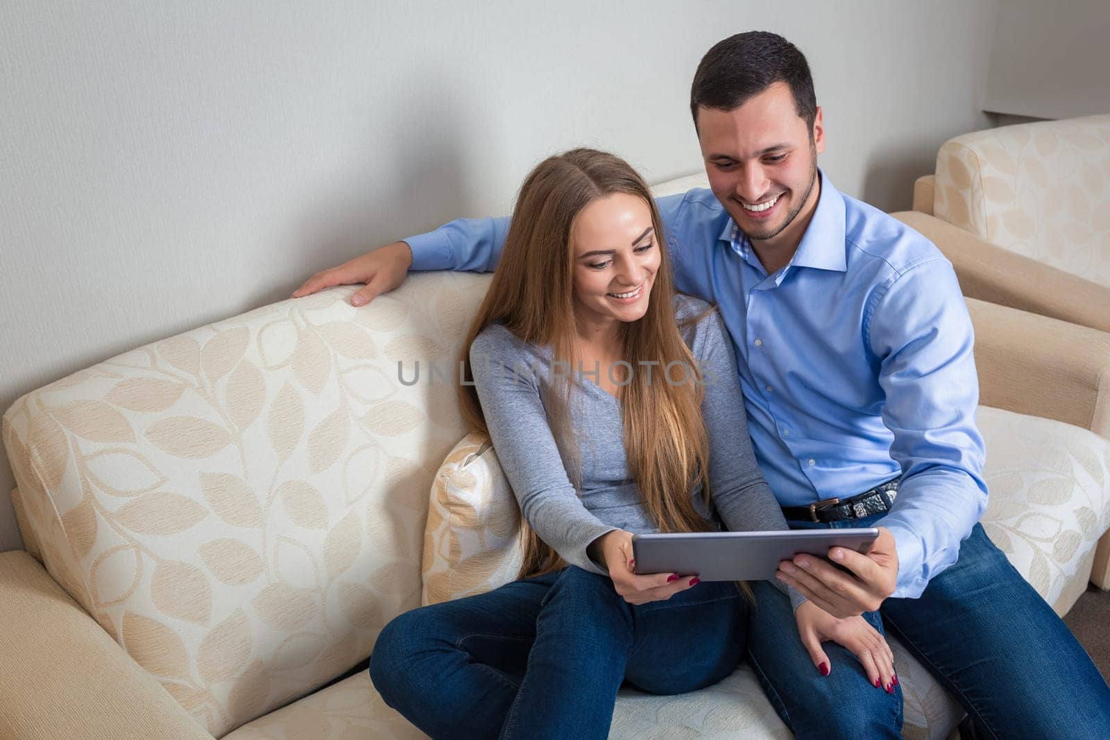 Young lovely couple, laughing sitting on sofa with electronic tablet by nazarovsergey