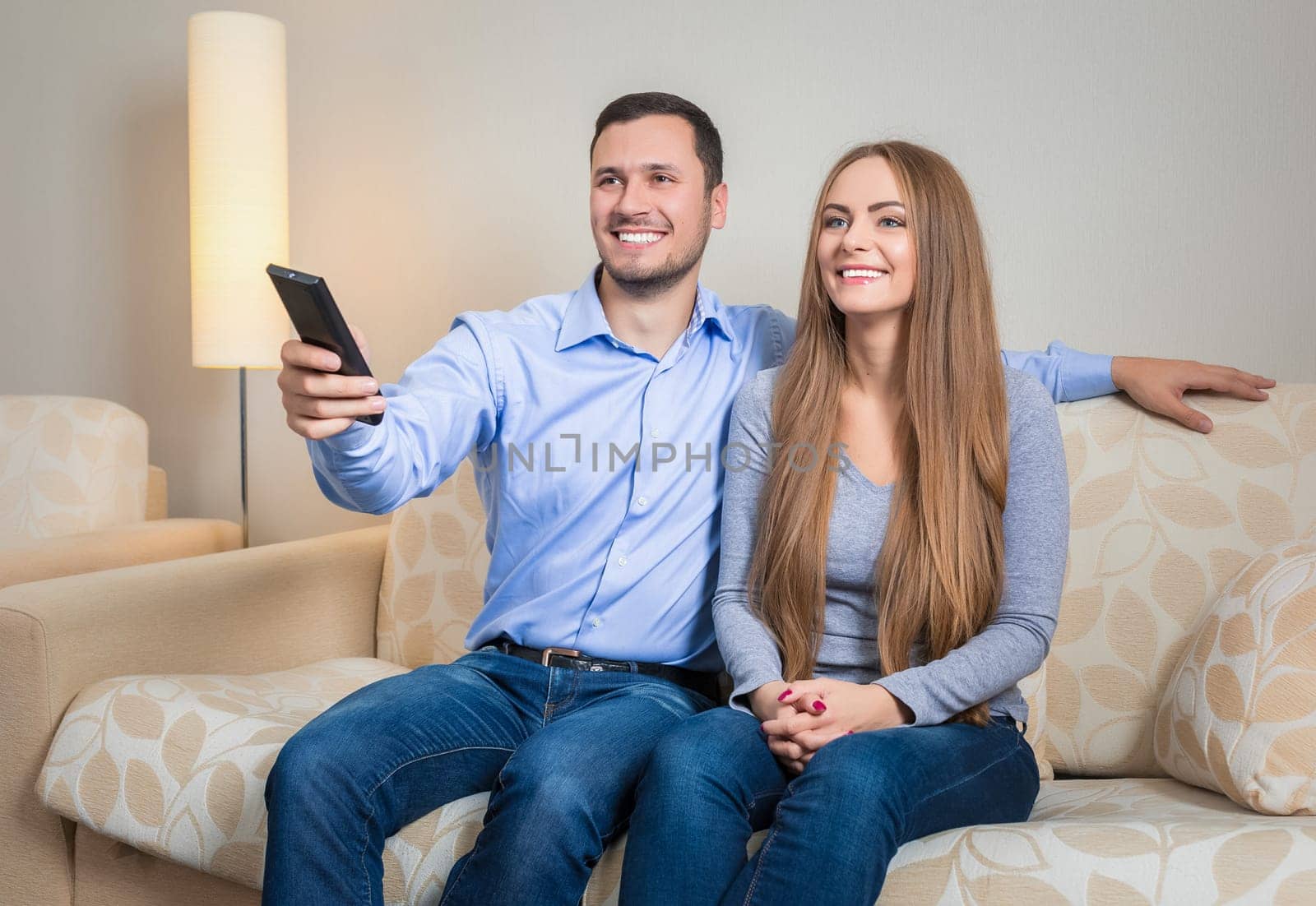 Portrait of happy couple sitting on sofa watching television together by nazarovsergey