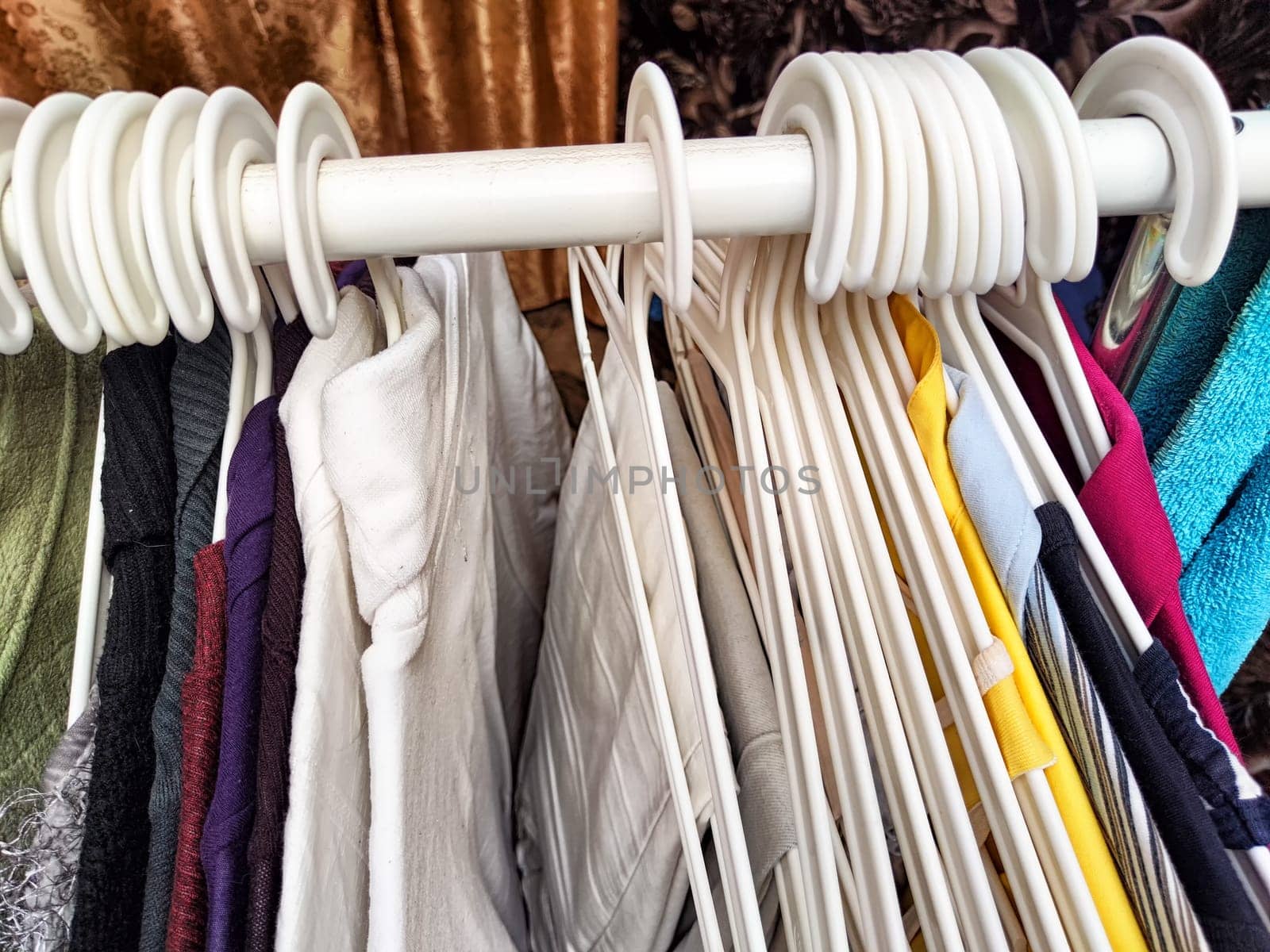 Hangers with a variety of clothes on white rack. Home storage of clothes. Clutter. Littery. Declutter. Garage sale