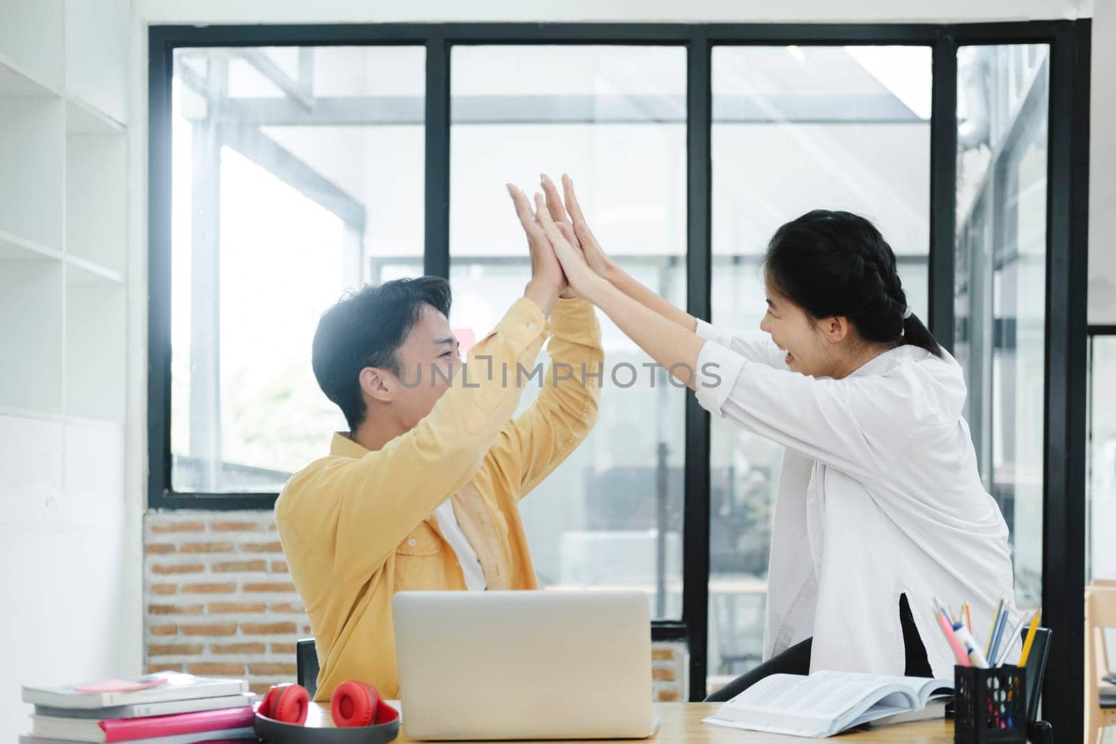 Two happy friendly colleague giving high five standing in office celebrating success, good cooperation result, partnership teamwork and team motivation in office work.