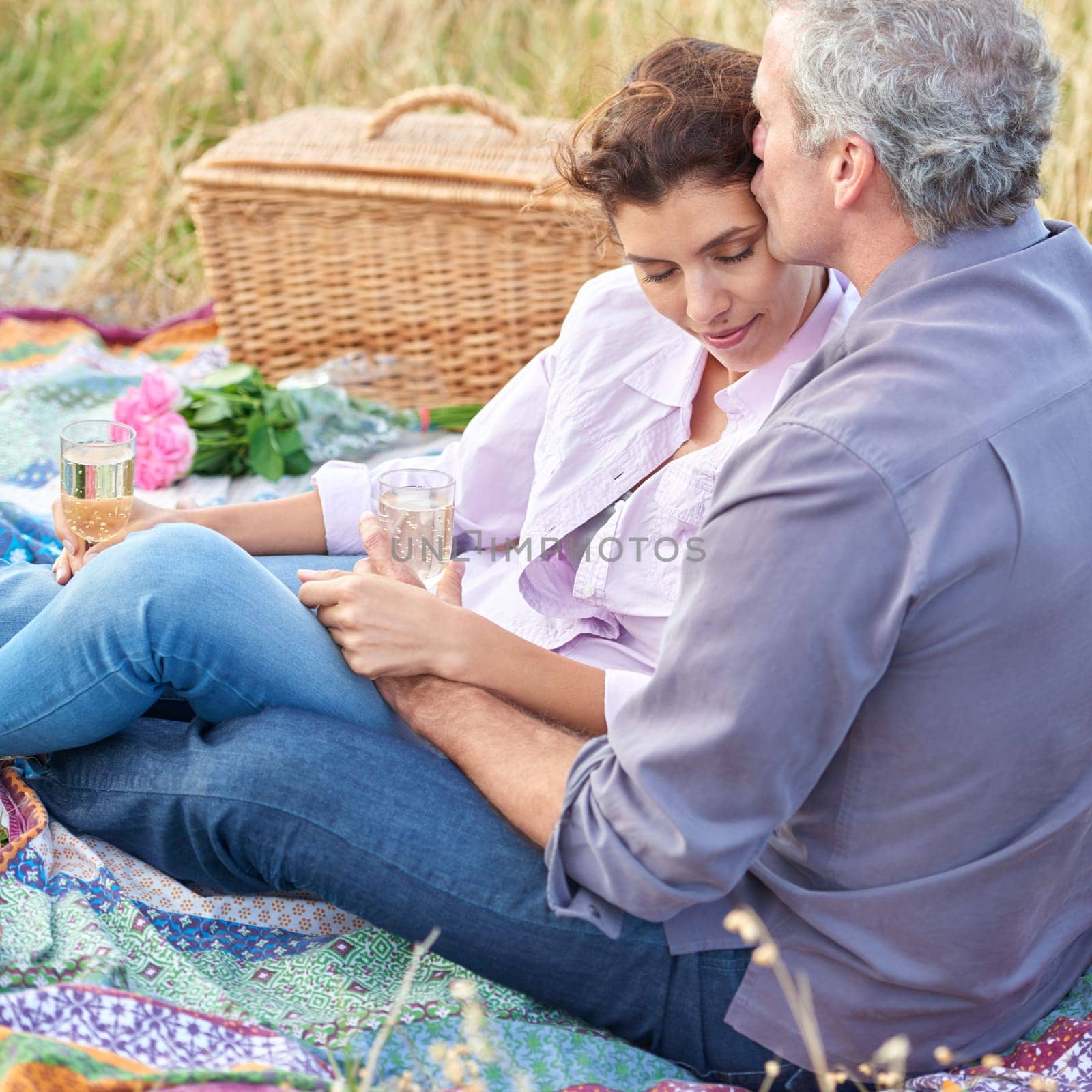 Kiss, senior couple and picnic in park, grass and basket in nature for a date or celebration with love and care. Mature, woman and man in field in summer, holiday or vacation with wine or drinks.