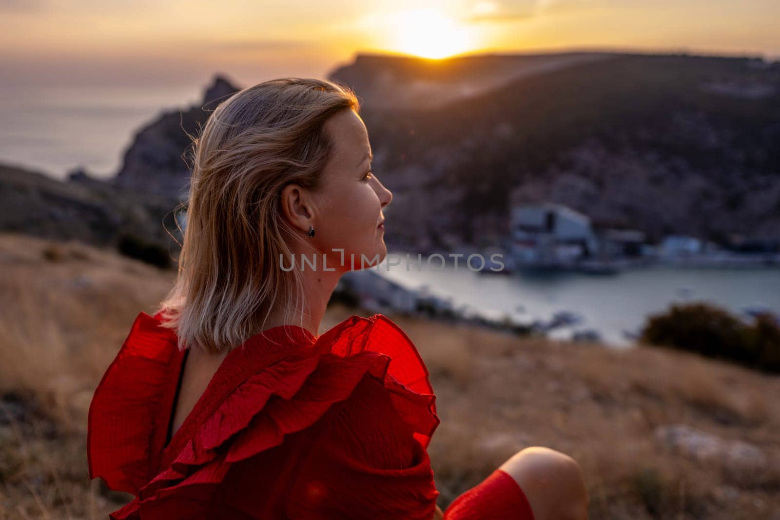 Woman sunset sea mountains. Happy woman siting with her back on the sunset in nature in summer posing with mountains on sunset, silhouette. Woman in the mountains red dress, eco friendly, summer landscape active rest.