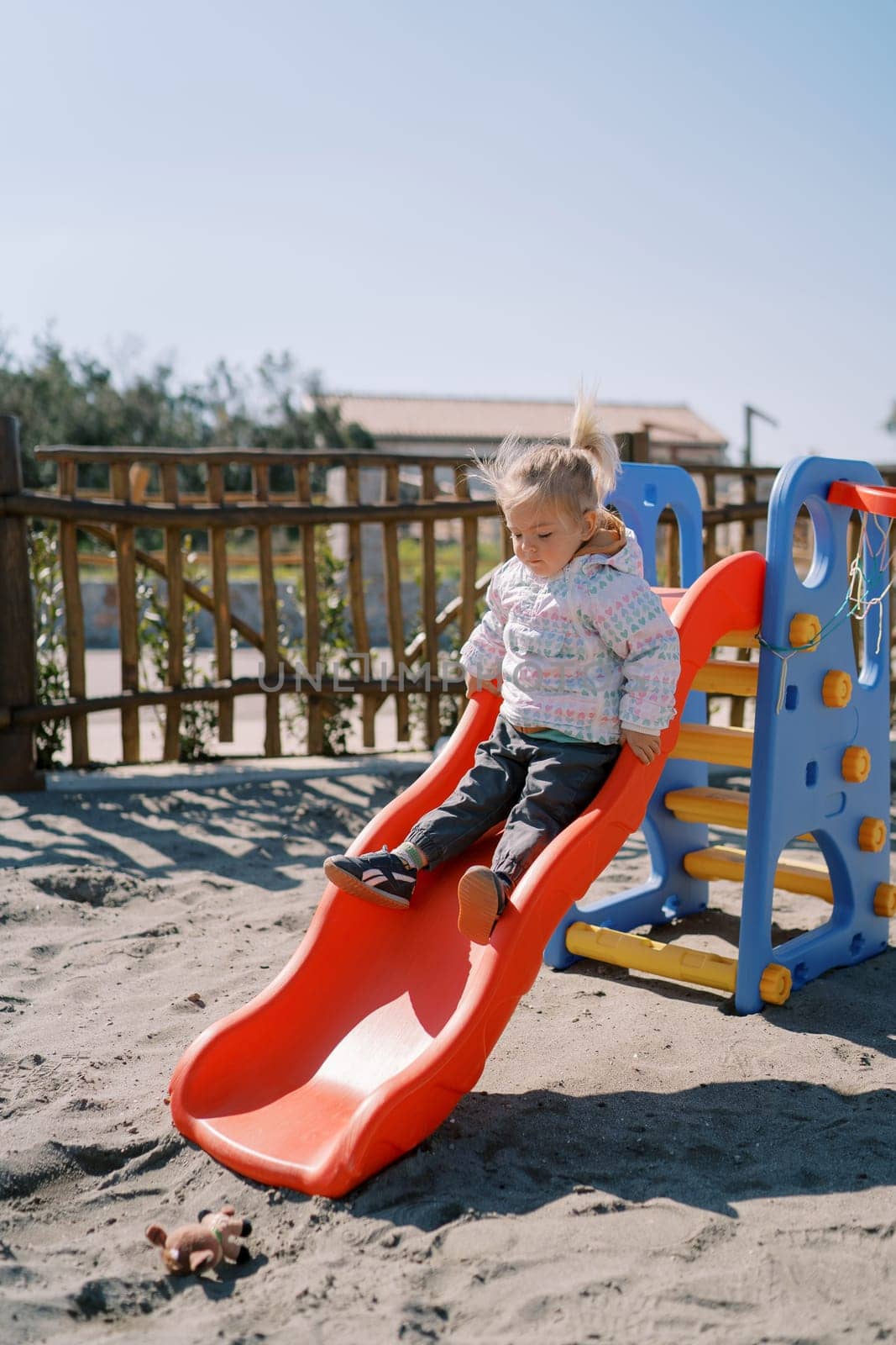 Little girl slides down a slide on the playground holding onto the handrails. High quality photo