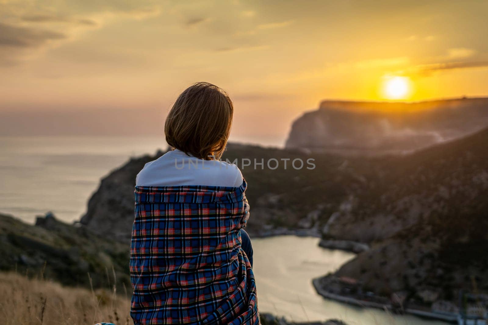 Happy woman on sunset in mountains. Woman siting with her back on the sunset in nature in summer. Silhouette. by Matiunina