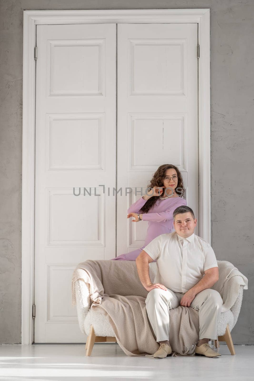 Young happy couple sitting on a sofa in a large studio. Behind them is a large white door. Loving married couple. Cope space for text