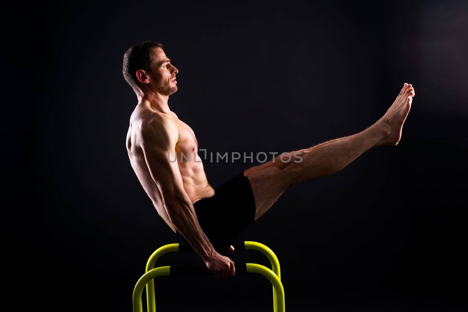 Male gymnast performing handstand on a parallel bars, studio shot