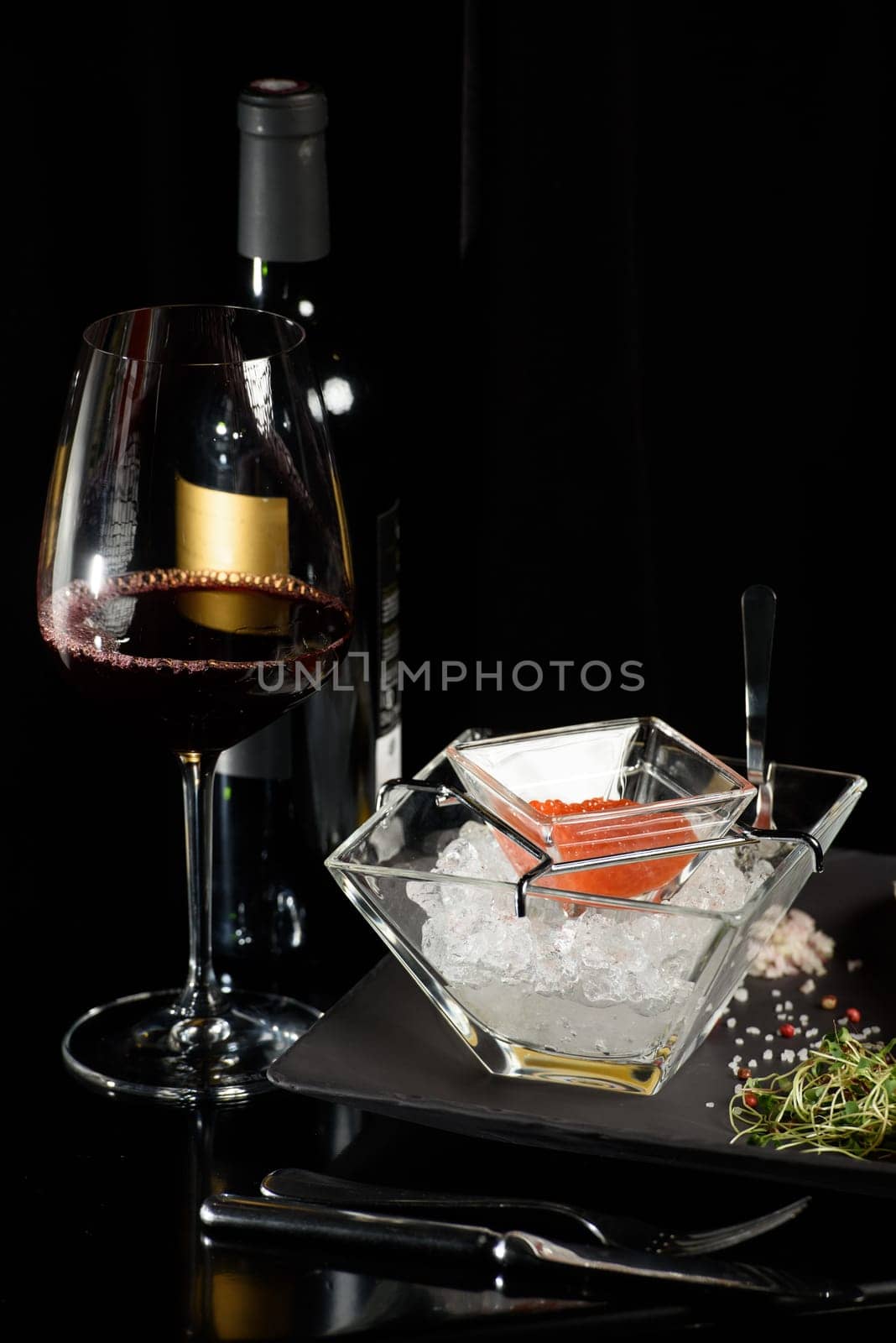 salmon fish caviar, on ice, with croutons and butter, on a transparent dish with a glass of red wine on a dark background