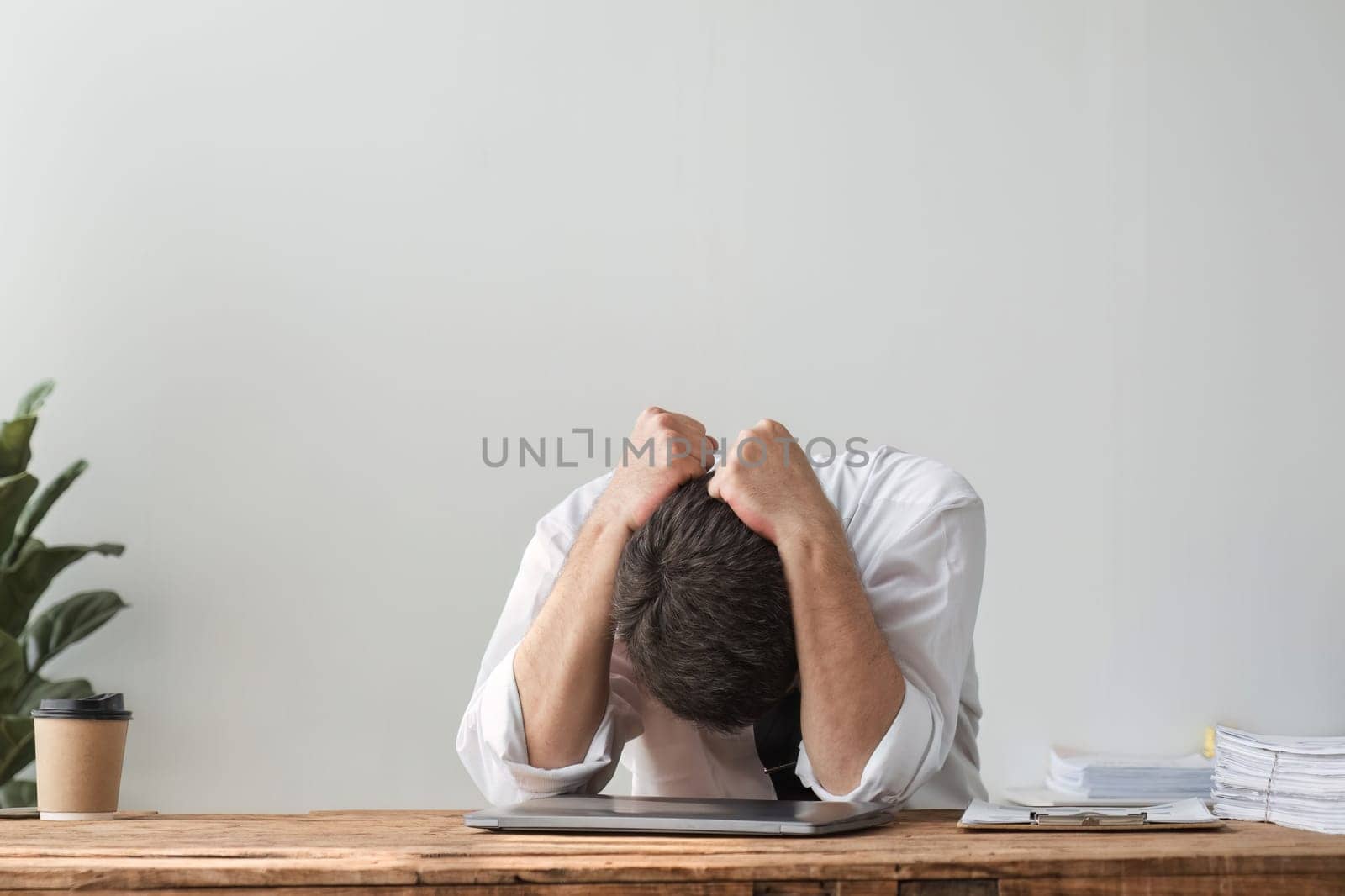 Unhappy young businessman feeling bored and stressed at work looking at laptop with hopeless expression while sitting in office by wichayada