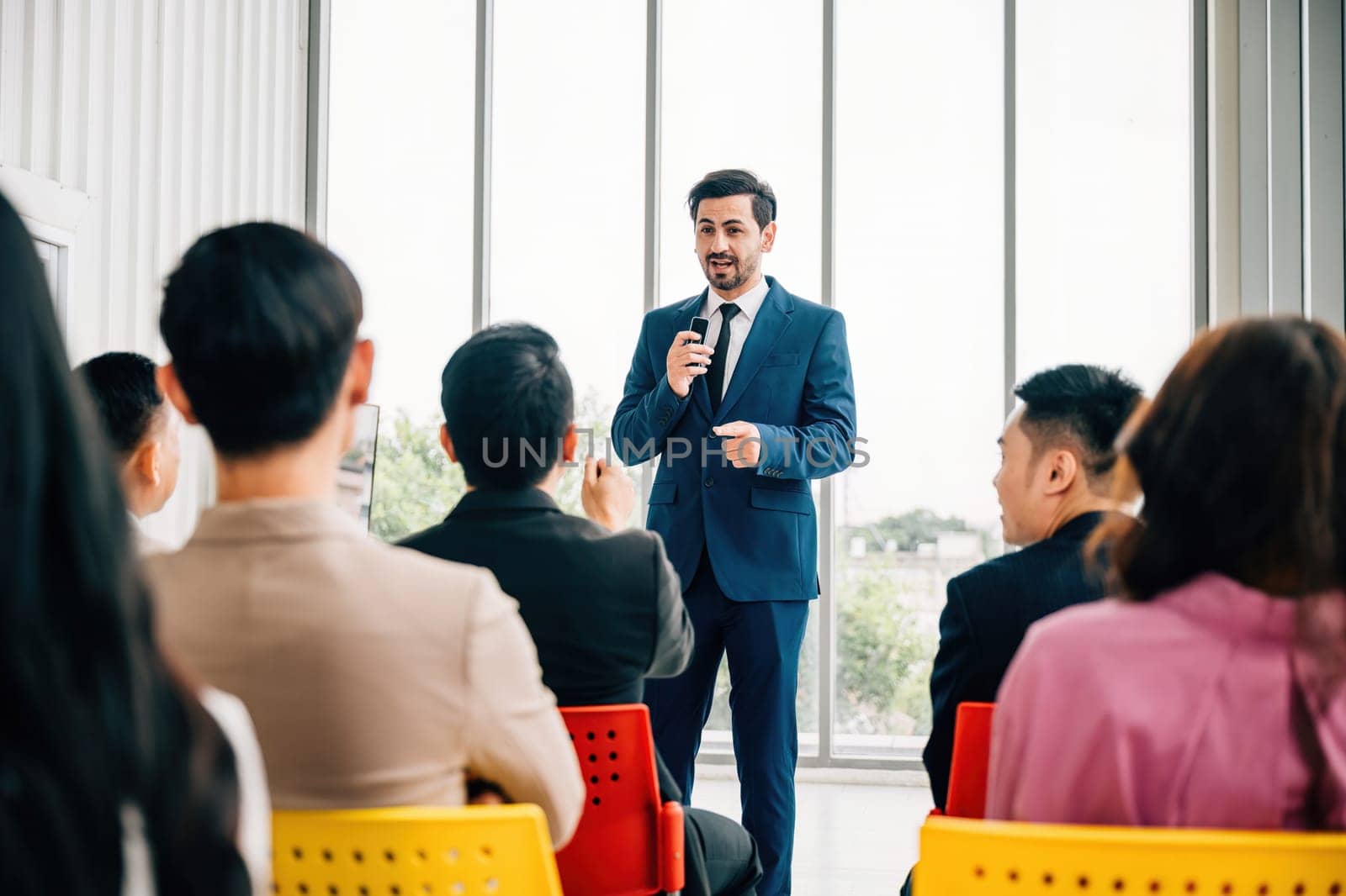 In a meeting room business professionals along with a diverse audience of colleagues sit and attentively listen as leaders present reviews. symbolizes importance of teamwork and collaborative success. by Sorapop