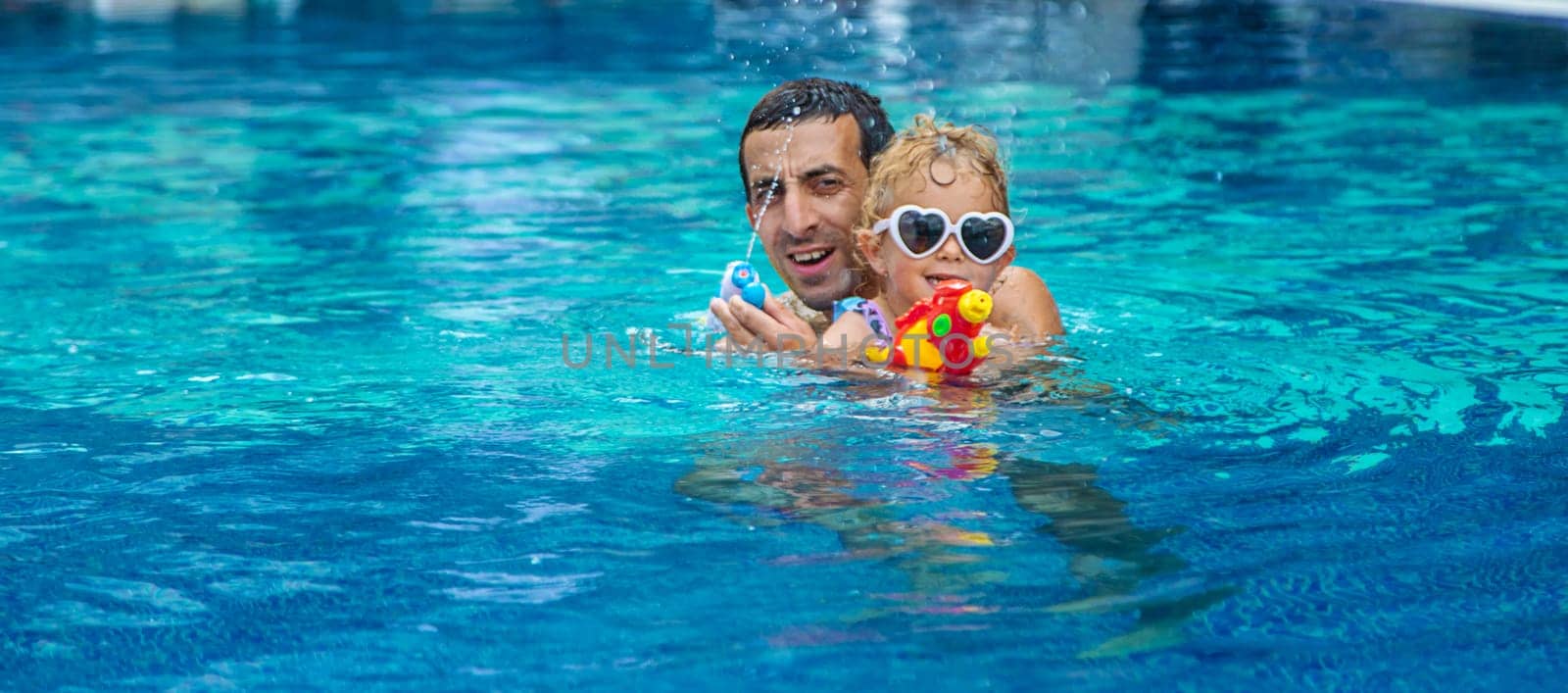 A child and his father play with a water pistol in the water. Selective focus. by yanadjana