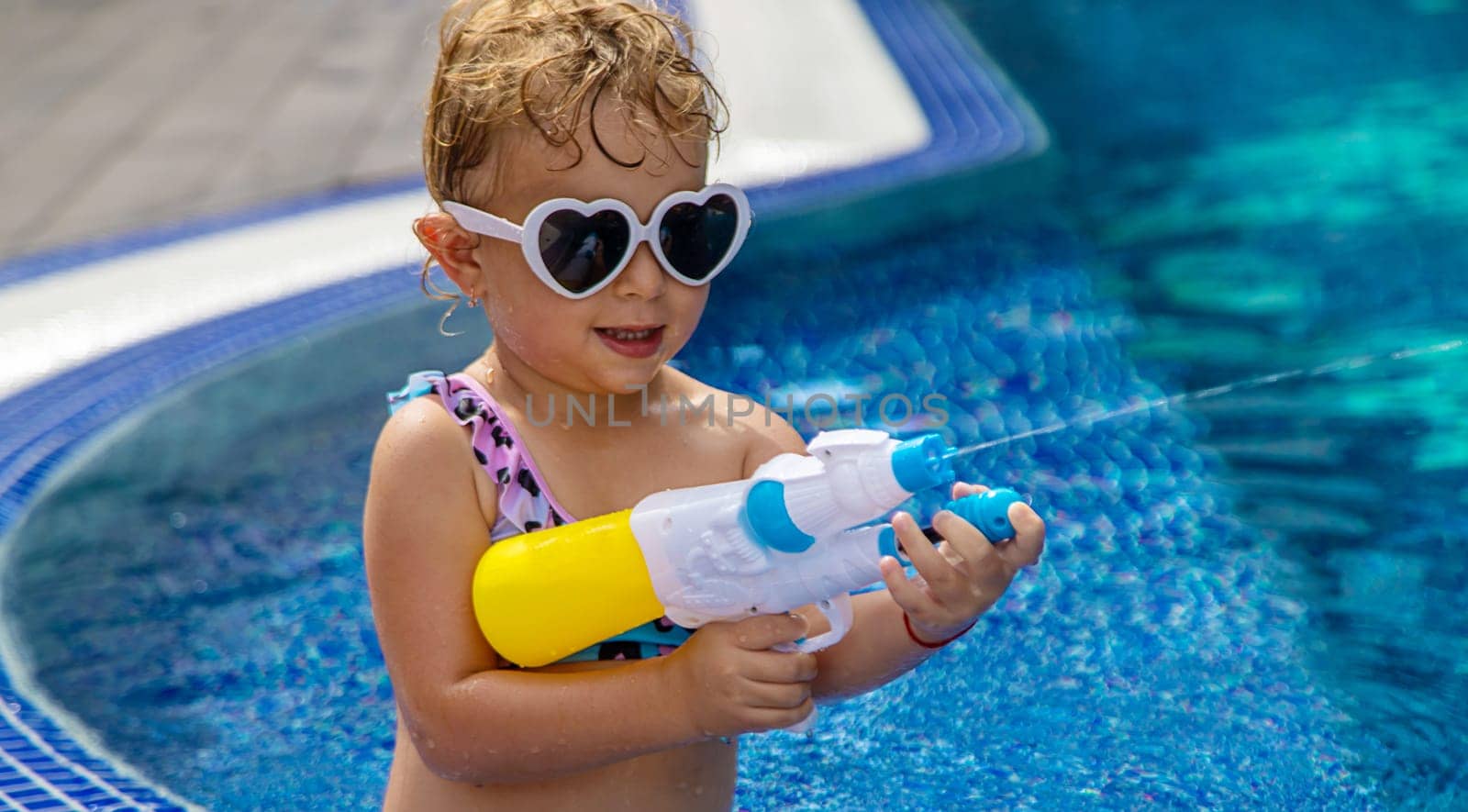 A child plays with a water pistol in the pool. Selective focus. by yanadjana