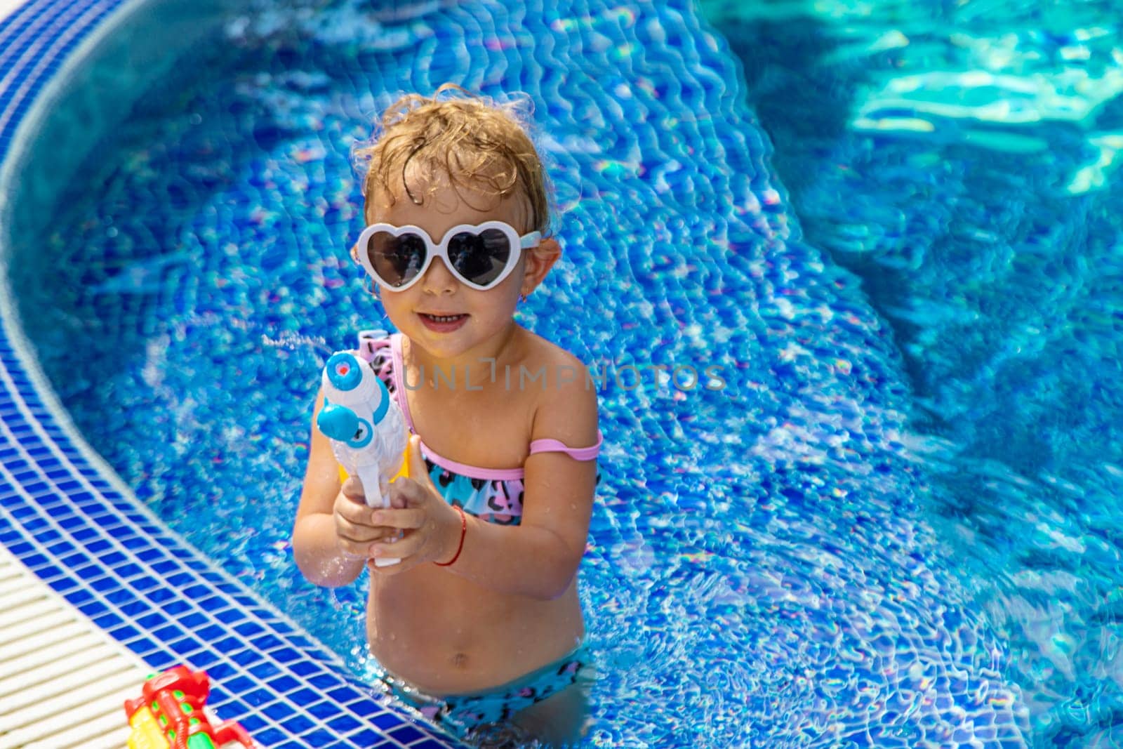 A child plays with a water pistol in the pool. Selective focus. Kid.