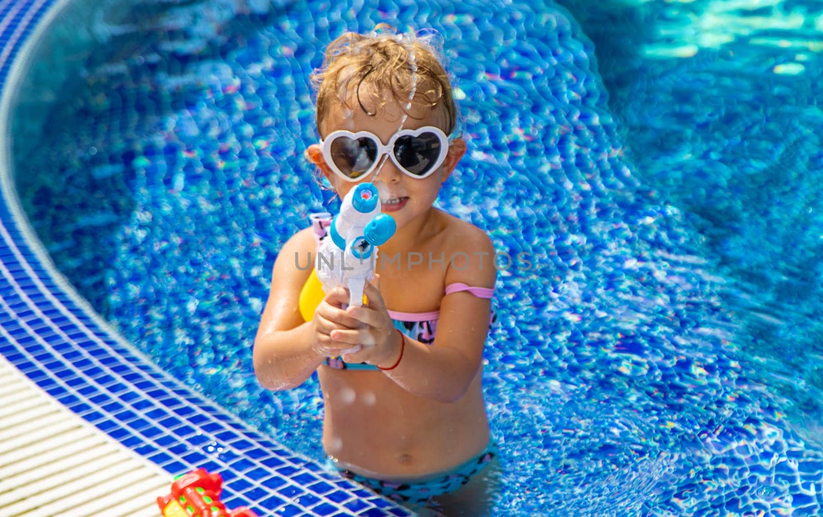 A child plays with a water pistol in the pool. Selective focus. by yanadjana