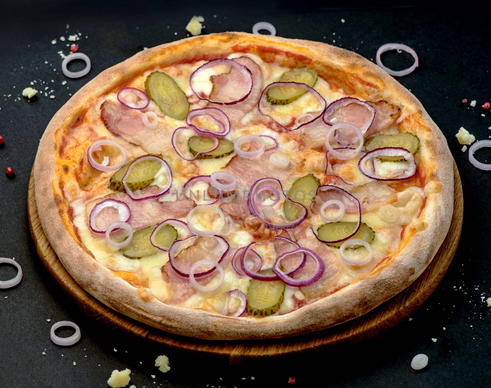 Pizza with cheese, ham, pickled cucumber and onion rings on a black background. Delicious pizza with meat and cheese by aprilphoto