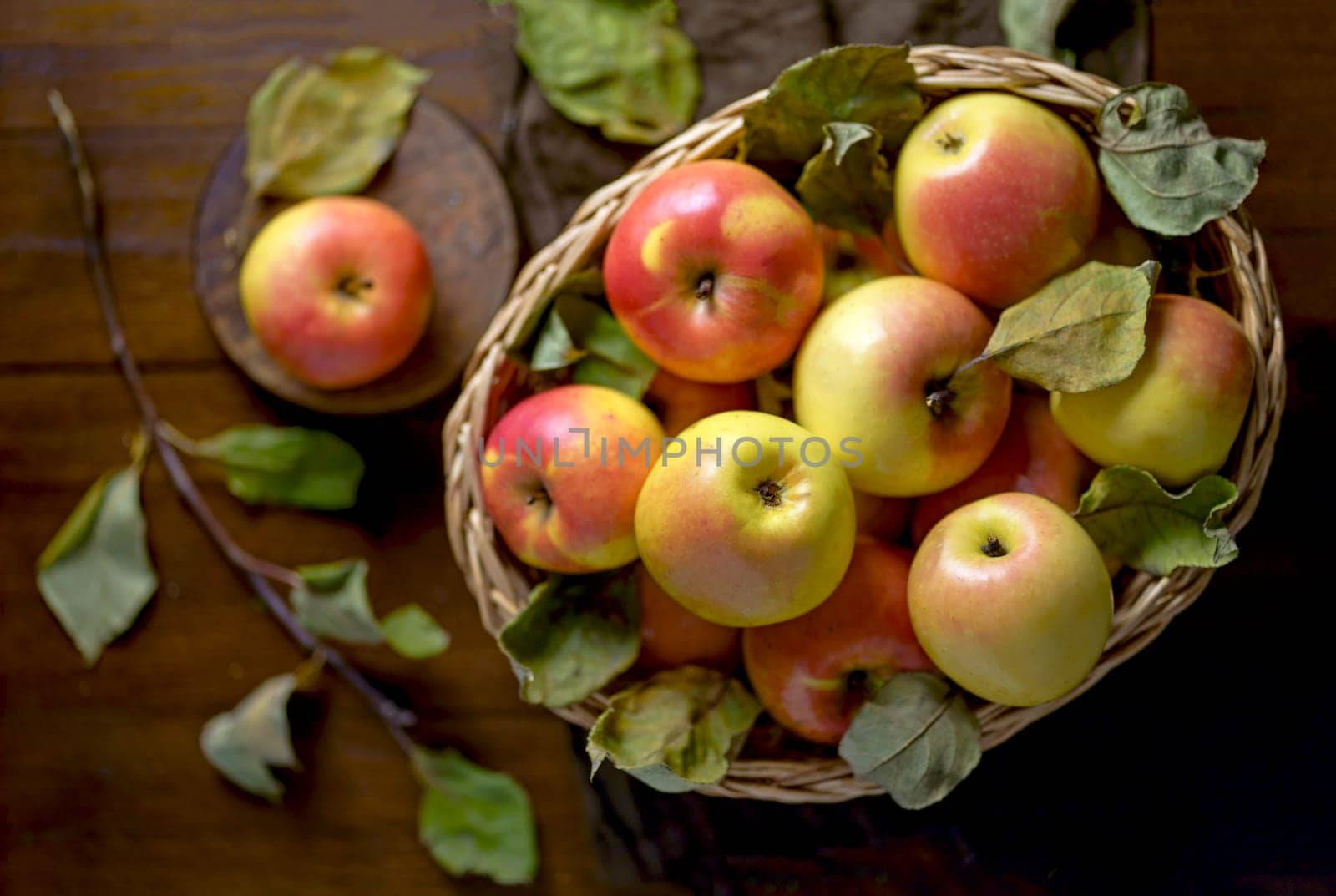 Apples in a basket on a wooden table. Fresh red apples with green leaves on a black background. Fruits. View from above. by aprilphoto