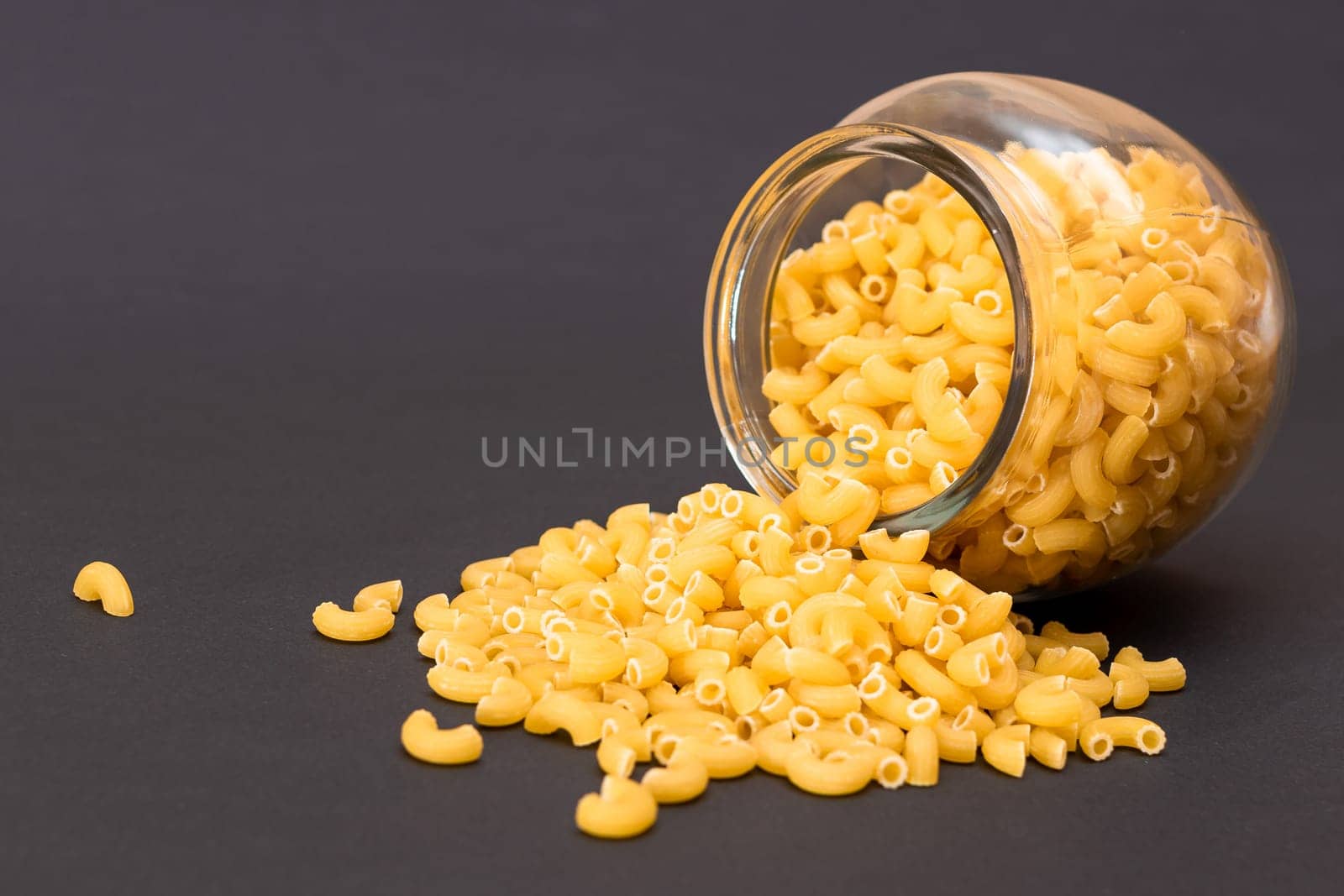 Uncooked Chifferi Rigati Pasta in Glass Jar on Black Background by InfinitumProdux