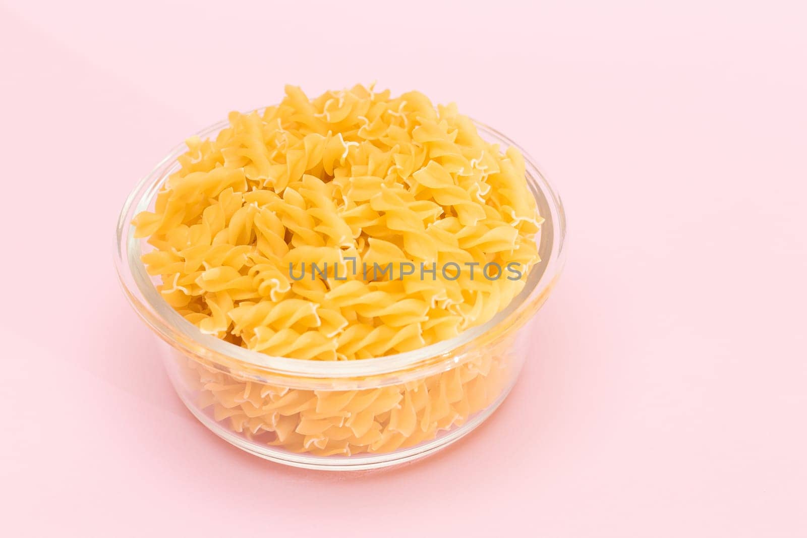 Uncooked Fusilli Pasta in Glass Jar on Pink Background by InfinitumProdux