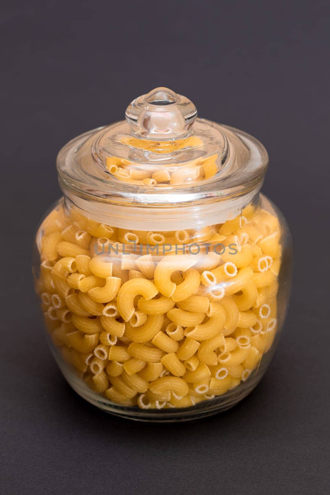 Uncooked Chifferi Rigati Pasta in Glass Jar on Black Background. Fat and Unhealthy Food. Classic Dry Macaroni. Italian Culture and Cuisine. Raw Pasta