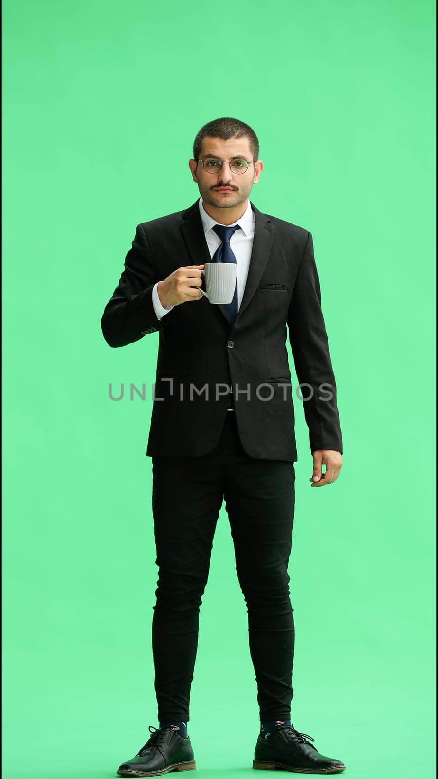 young man in full growth. isolated on green background. holding a mug of coffee.