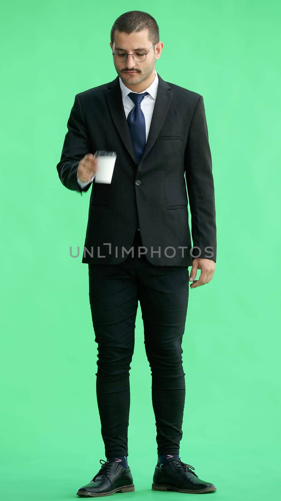 young man in full growth. isolated on green background. holding a mug of coffee.