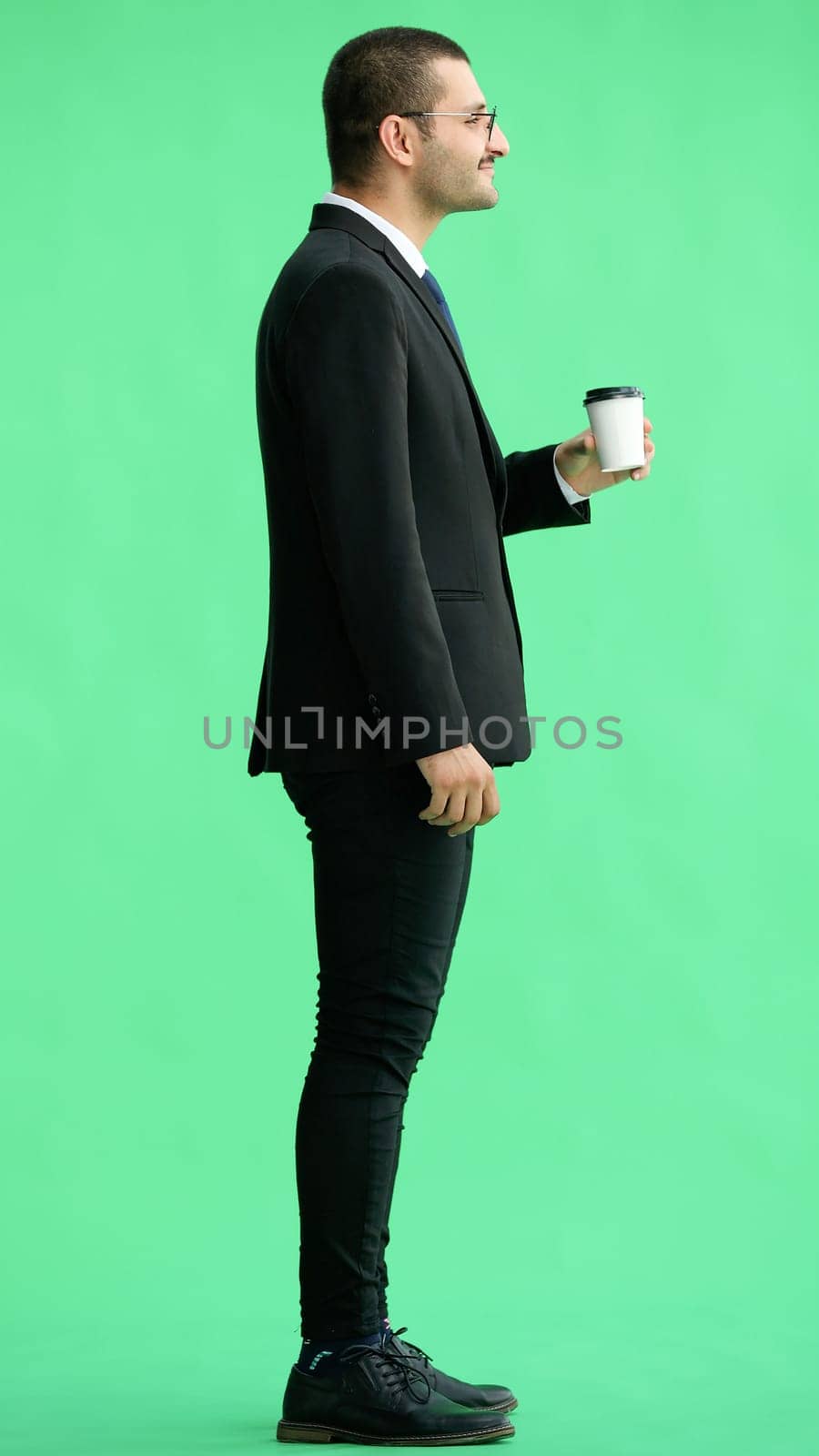 young man in full growth. isolated on green background. holding a mug of coffee.