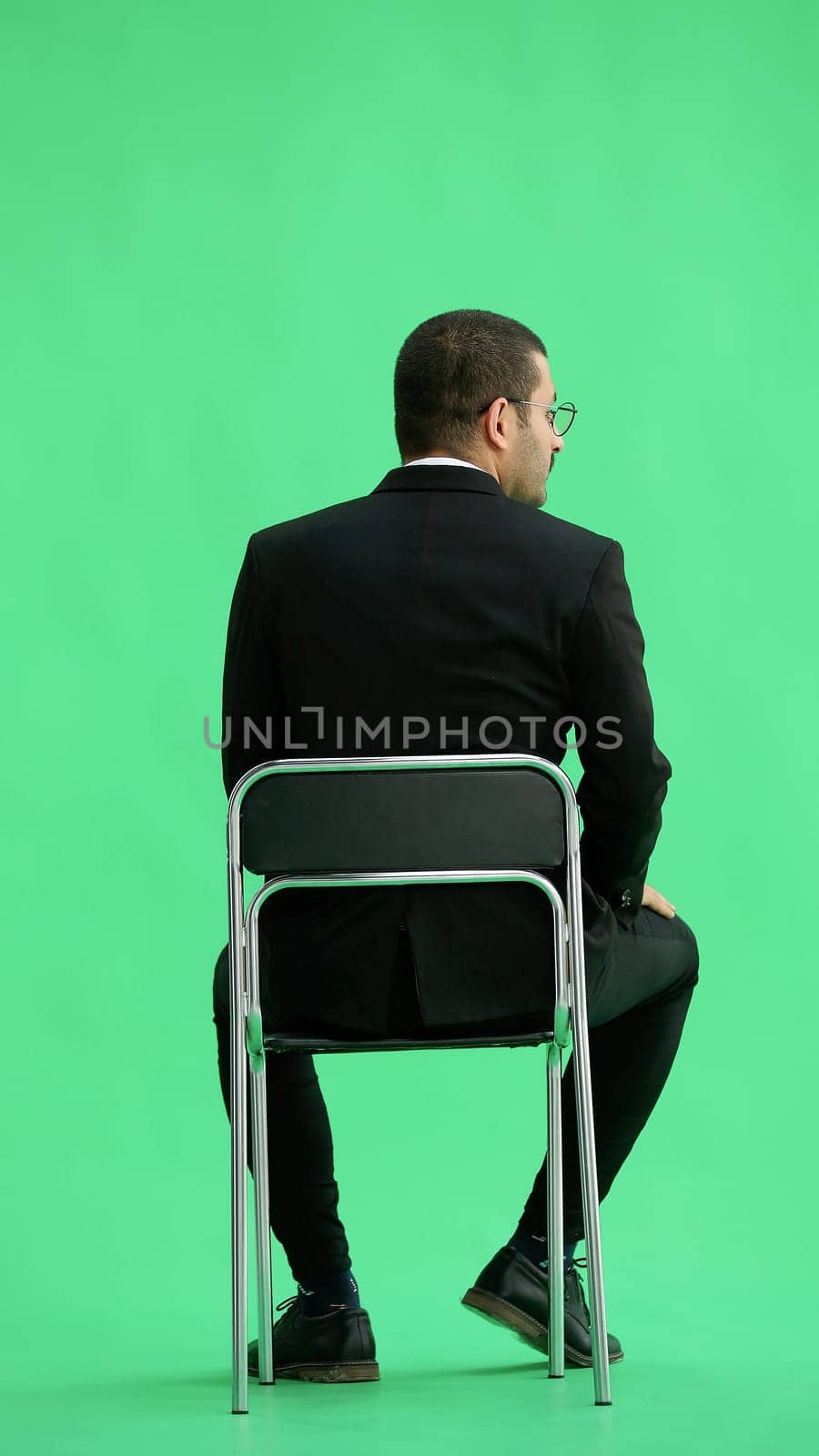 young man in full growth. isolated on a green background sitting on a chair by Prosto