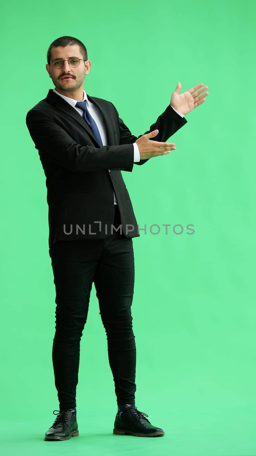 young man in full growth. isolated on a green background shows hands to the side by Prosto
