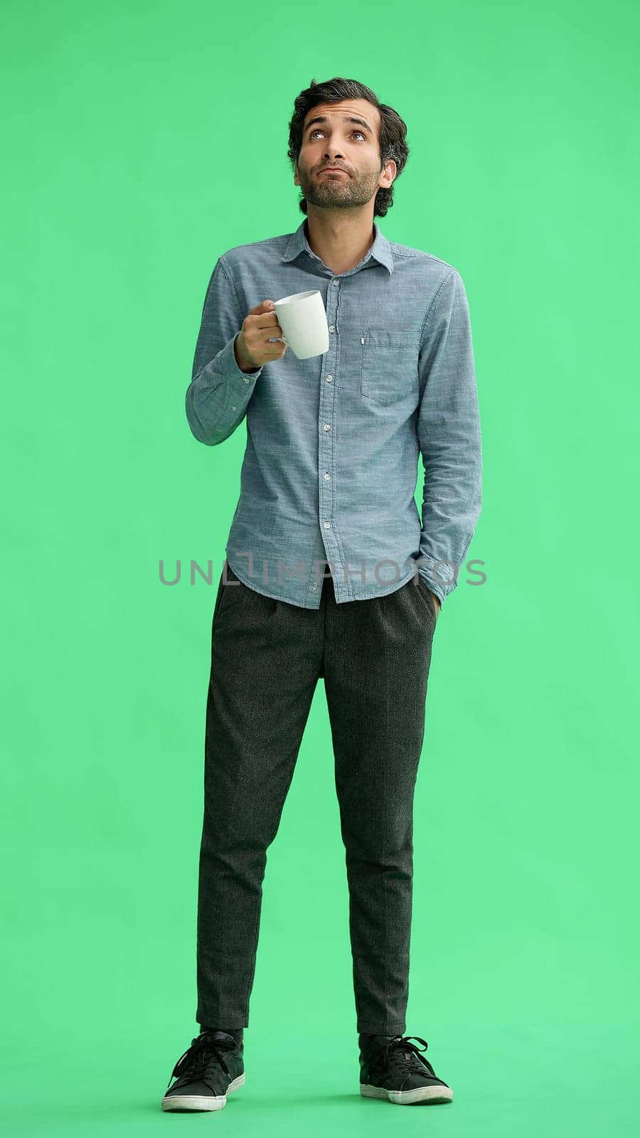 young man in full growth. isolated on green background. holding a mug of coffee.
