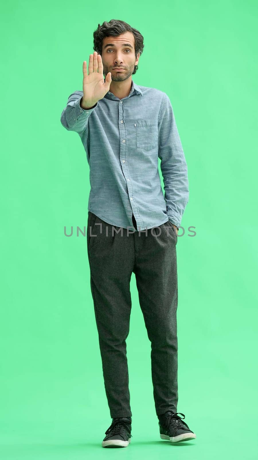 man in full growth. isolated on green background shows stop sign with hand.